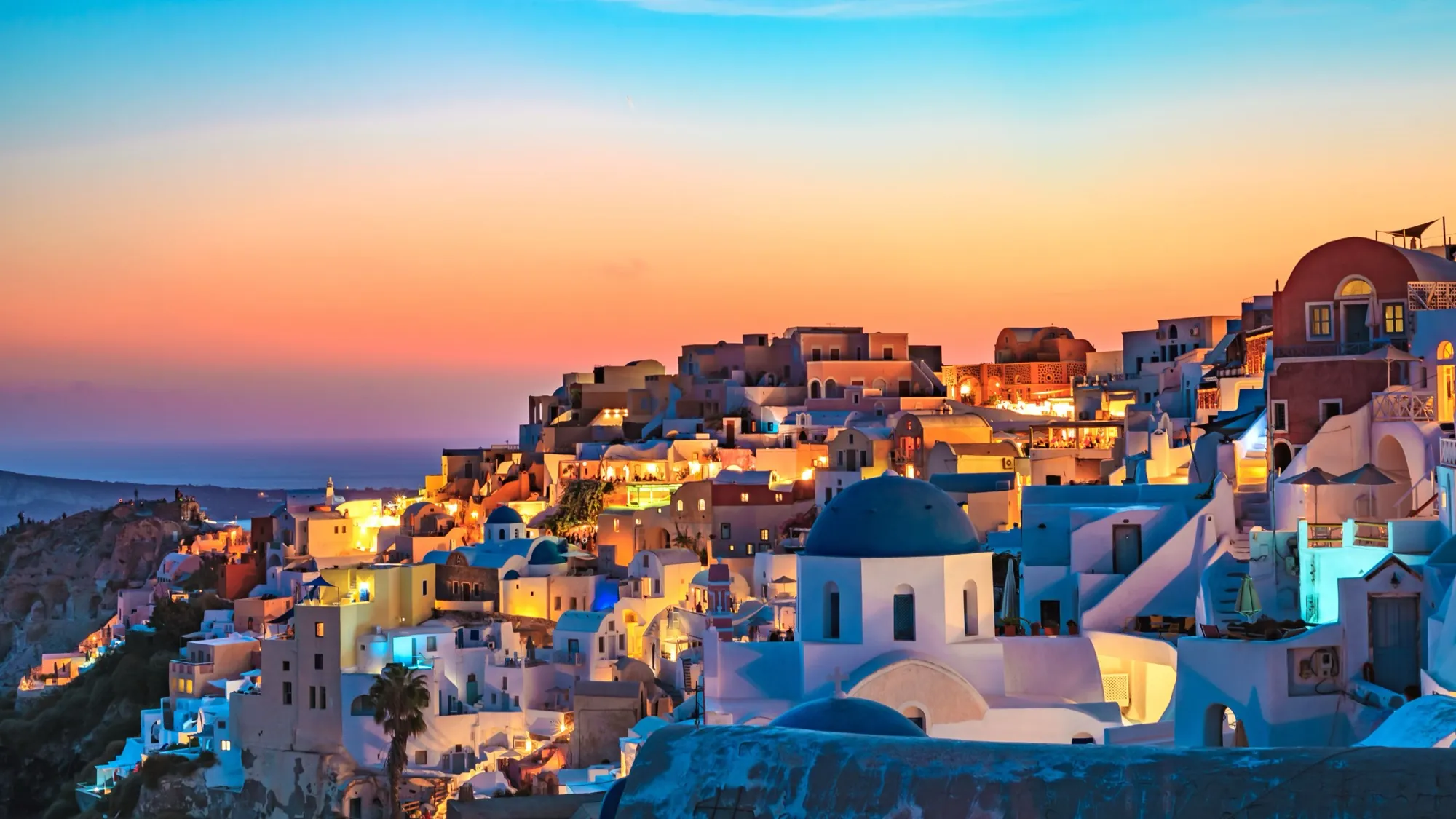 Whitewashed houses and blue domes of Oia, Santorini, lit up at sunset above the sea