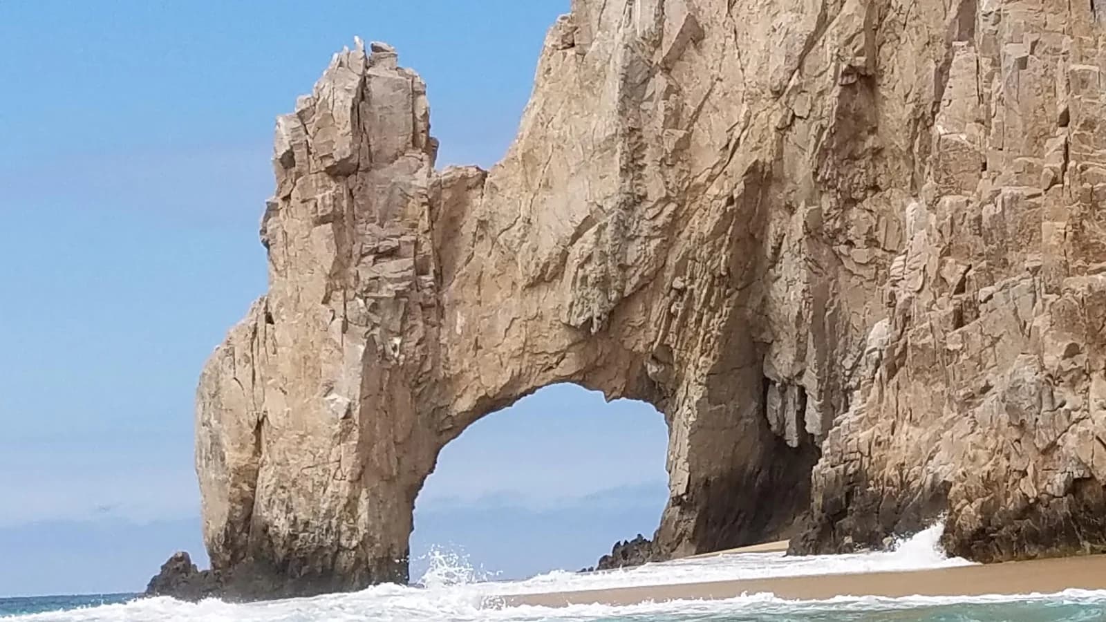 El Arco, the Land's End rock arch at Cabo San Lucas, with waves on the beach under a sunny sky