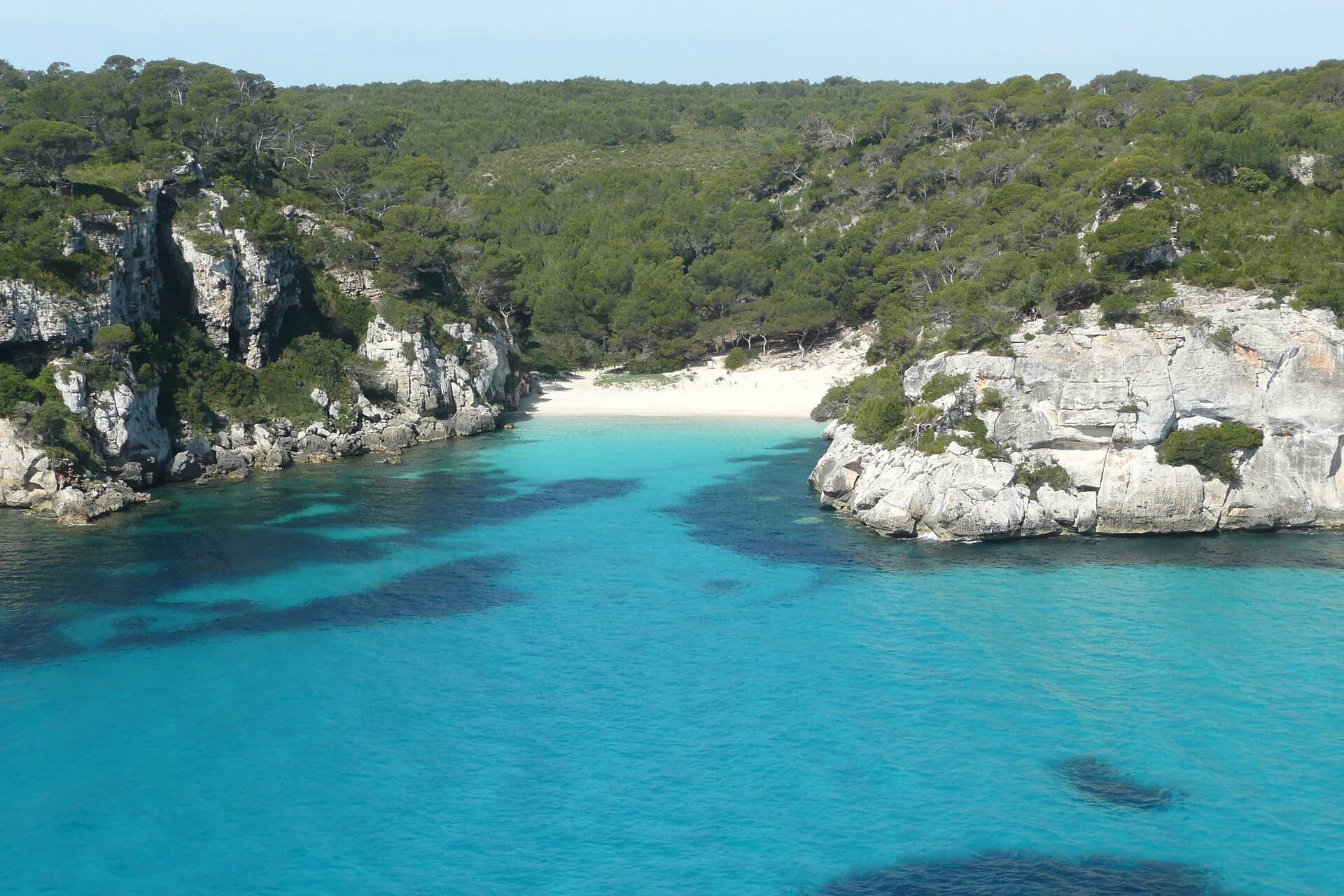Cala Macarelleta, Menorca, Spain — elevated overview of the small cove and turquoise water framed by pine-covered cliffs