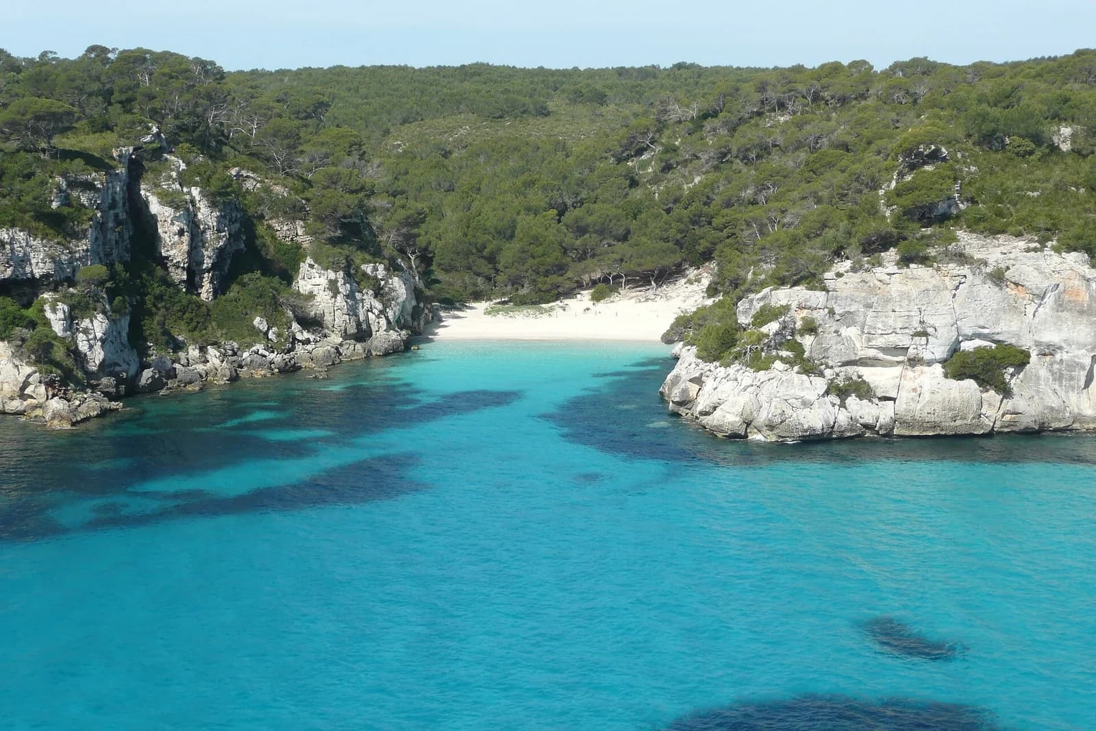 Cala Macarelleta, Menorca, Spain - elevated overview of the small cove and turquoise water framed by pine-covered cliffs