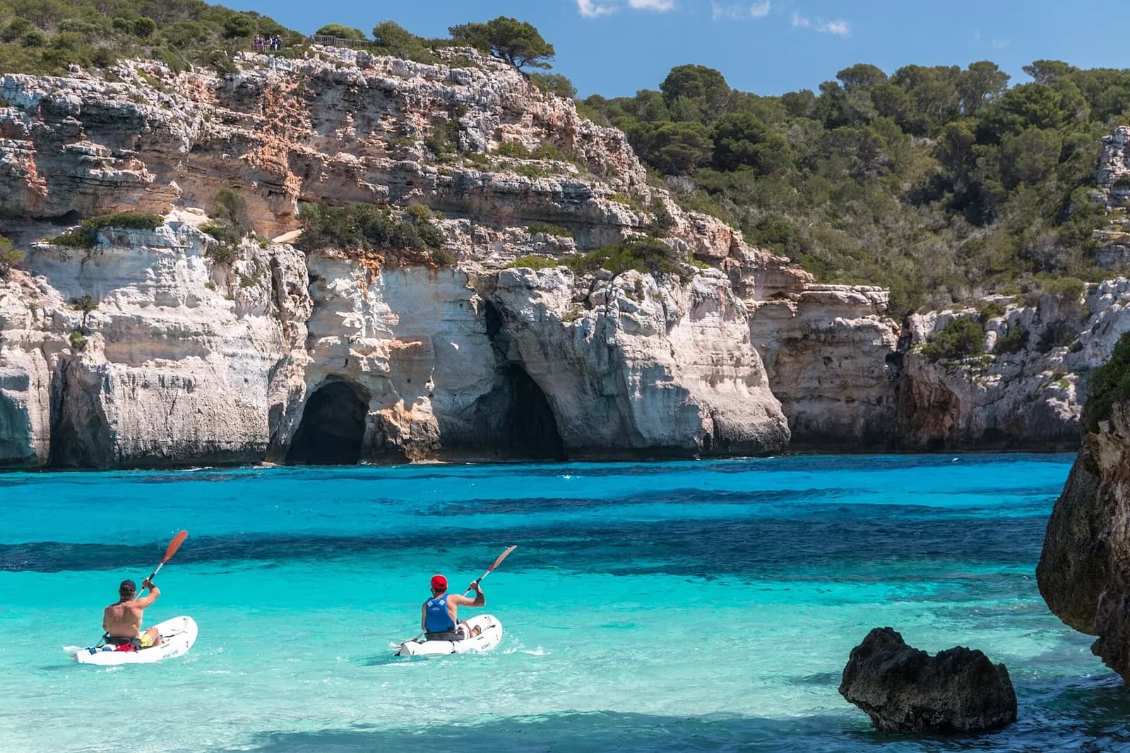 Cala Macarelleta, Menorca, Spain - kayakers on the clear water below the cove's limestone sea caves