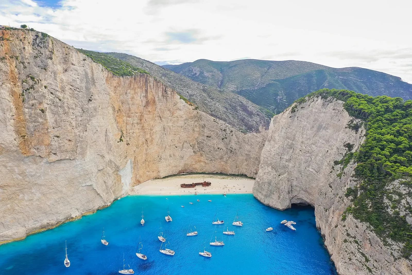 Navagio (Shipwreck) Beach, Zakynthos, Greece - aerial view of the cove with the wreck on the sand and yachts in turquoise water
