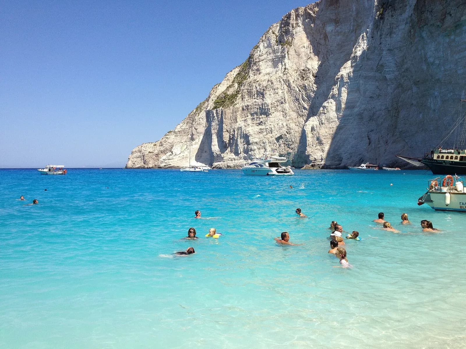 Navagio (Shipwreck) Beach, Zakynthos, Greece - turquoise shallows and white cliffs with swimmers off the beach