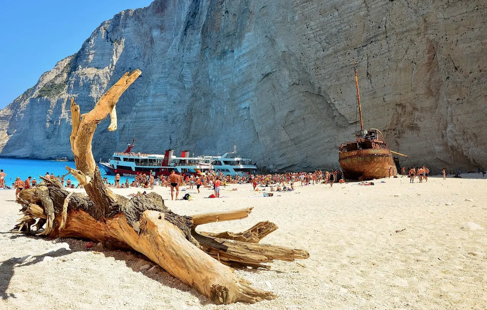 Navagio (Shipwreck) Beach, Zakynthos, Greece - beach-level view with weathered driftwood and the rusted shipwreck on white sand