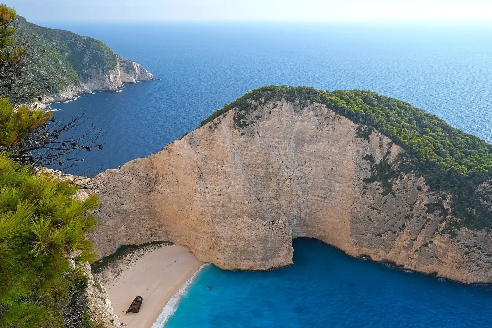 Navagio (Shipwreck) Beach, Zakynthos, Greece - cliff-top viewpoint over the cove framed by pine, with the wreck on the sand