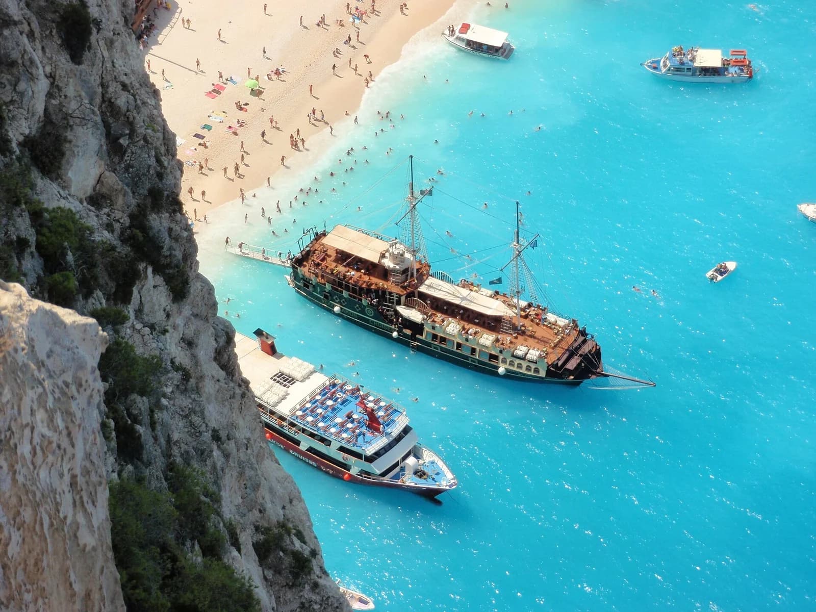 Navagio (Shipwreck) Beach, Zakynthos, Greece - tour boats and swimmers along the shoreline seen from the overlook above