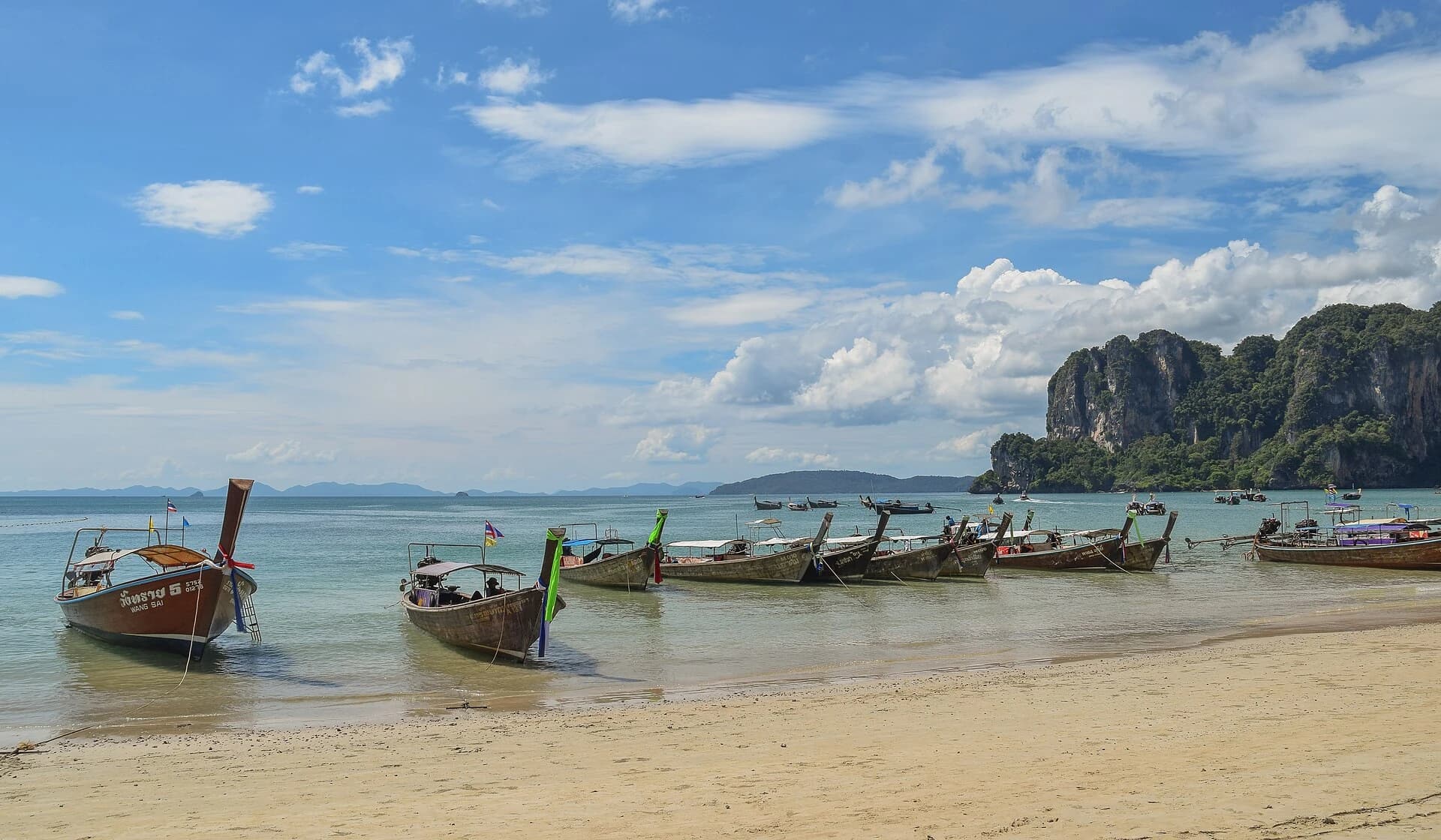 Railay Beach, Krabi, Thailand — longtail boats lined along the white sand of Railay West below limestone cliffs