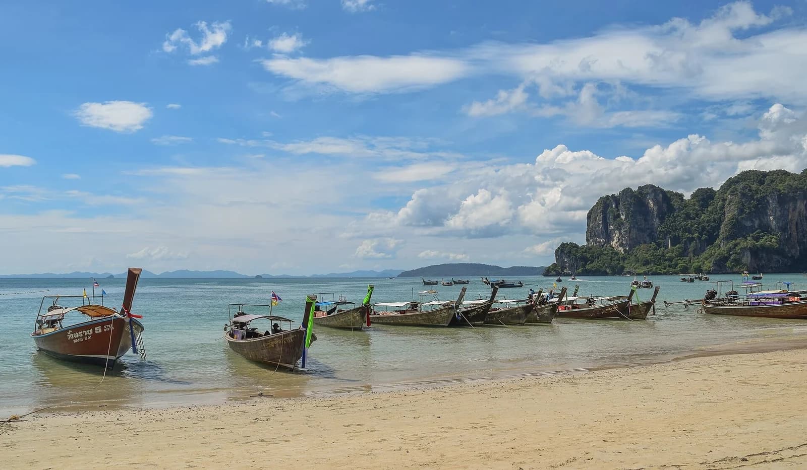 Railay Beach, Krabi, Thailand - longtail boats lined along the white sand of Railay West below limestone cliffs