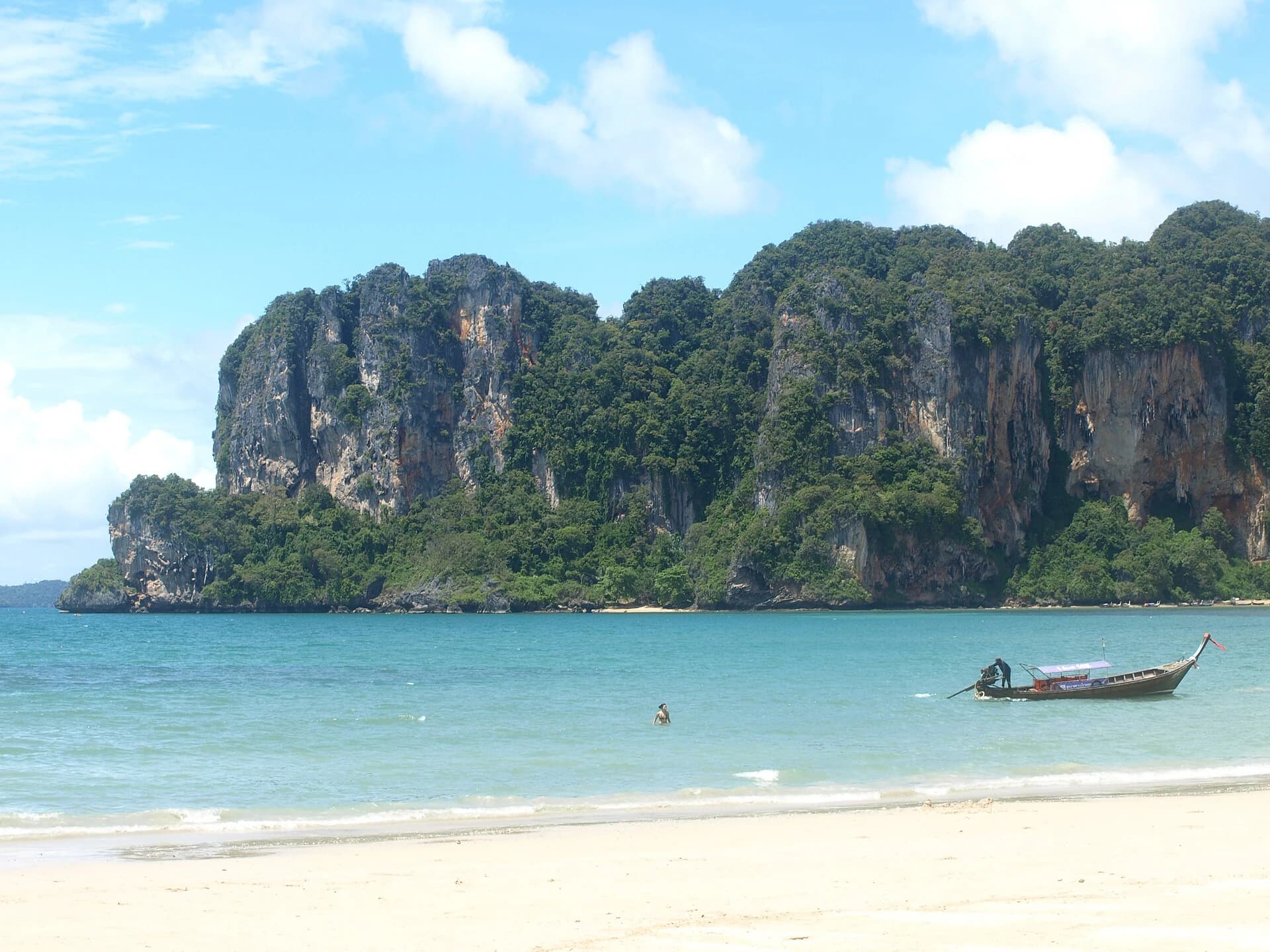 Railay Beach, Krabi, Thailand — turquoise shallows and white sand with a lone longtail boat below the cliffs