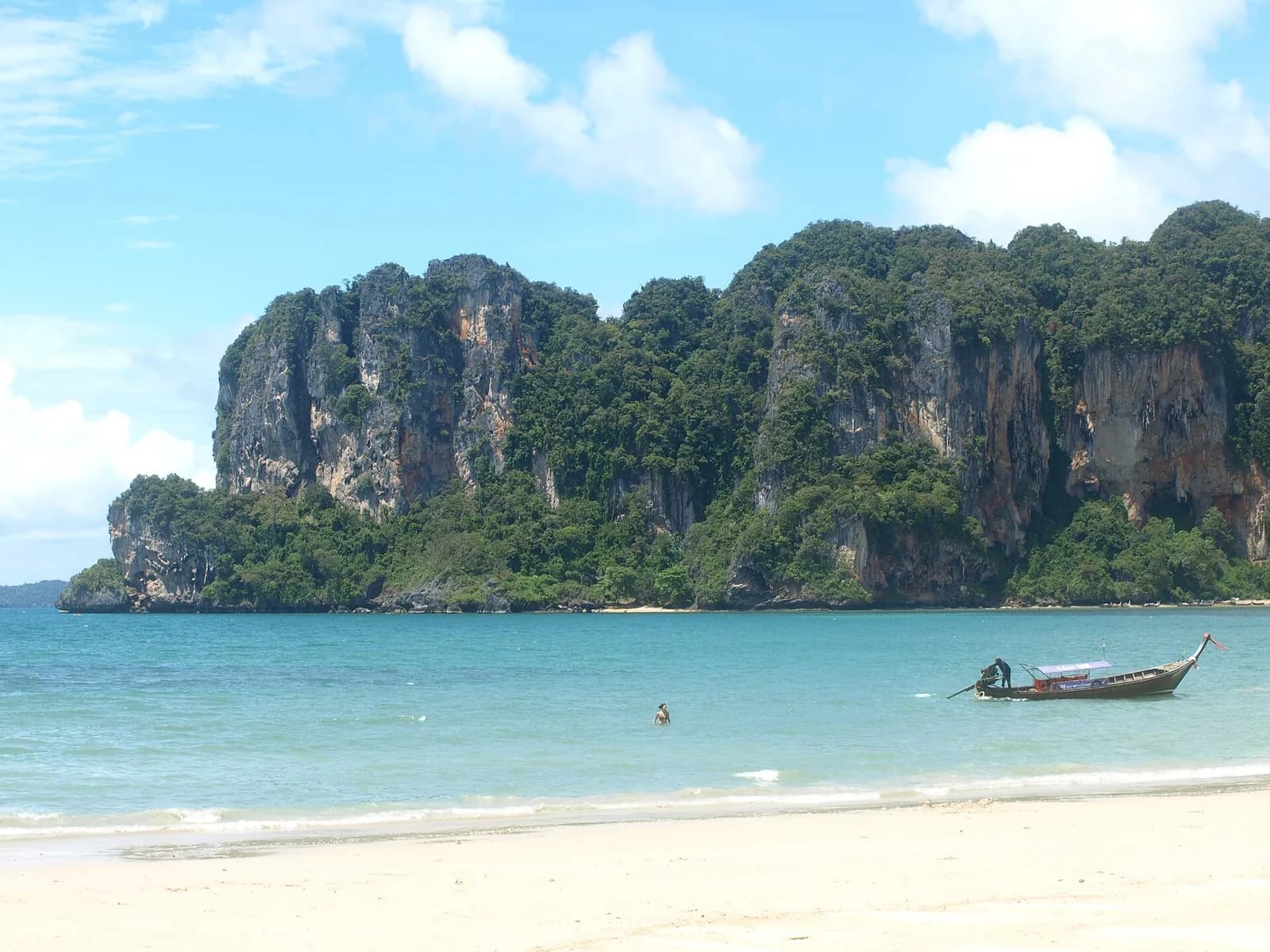 Railay Beach, Krabi, Thailand - turquoise shallows and white sand with a lone longtail boat below the cliffs