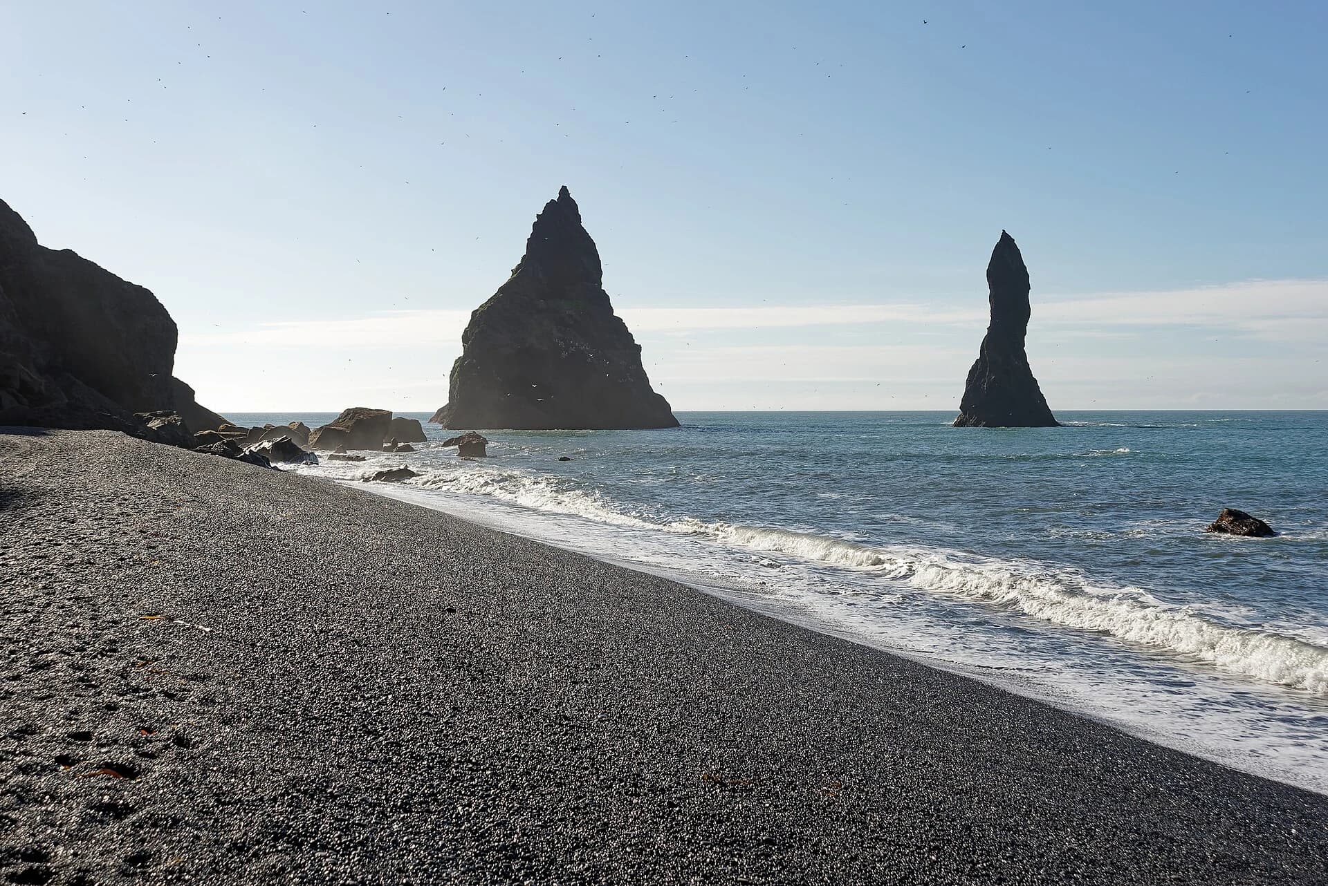 Reynisfjara, South Iceland — black volcanic sand in the foreground with the Reynisdrangar sea stacks and blue surf