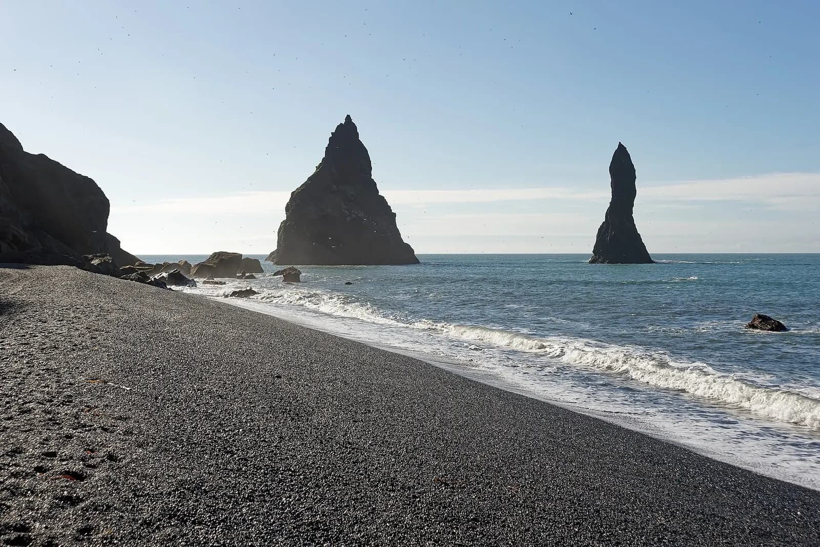 Reynisfjara, South Iceland - black volcanic sand in the foreground with the Reynisdrangar sea stacks and blue surf