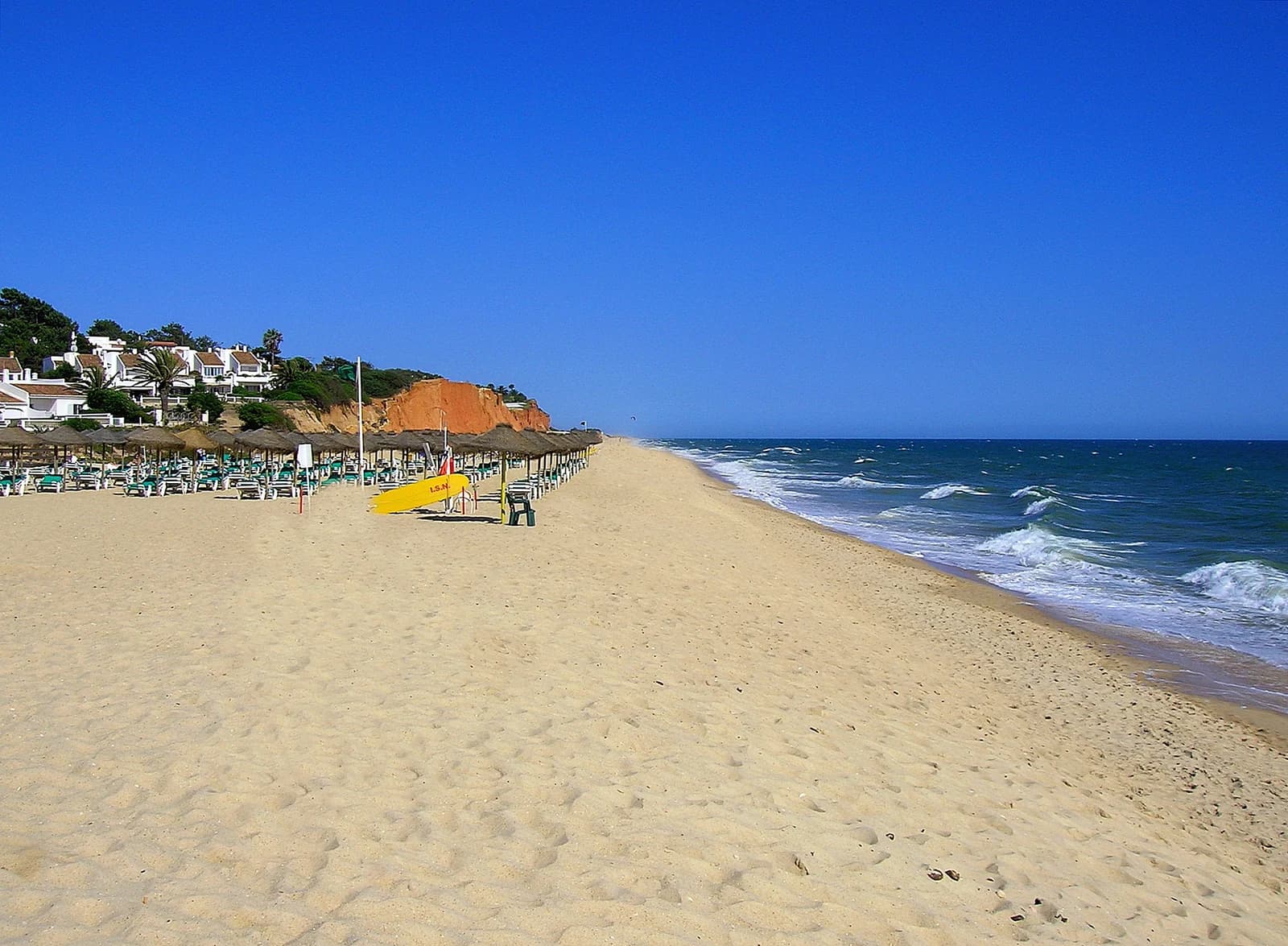 The long sandy beach at Vale do Lobo near Quinta do Lago, with parasols below the red cliffs