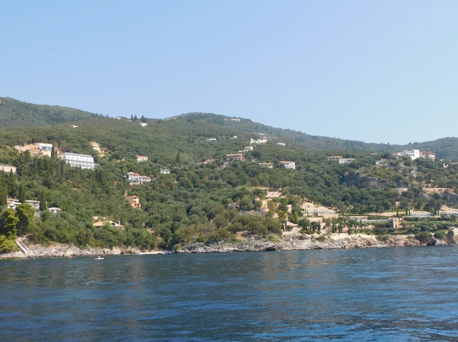 The olive-covered hillside and rocky shore at Nissaki on Corfu's north-east coast, seen from the sea