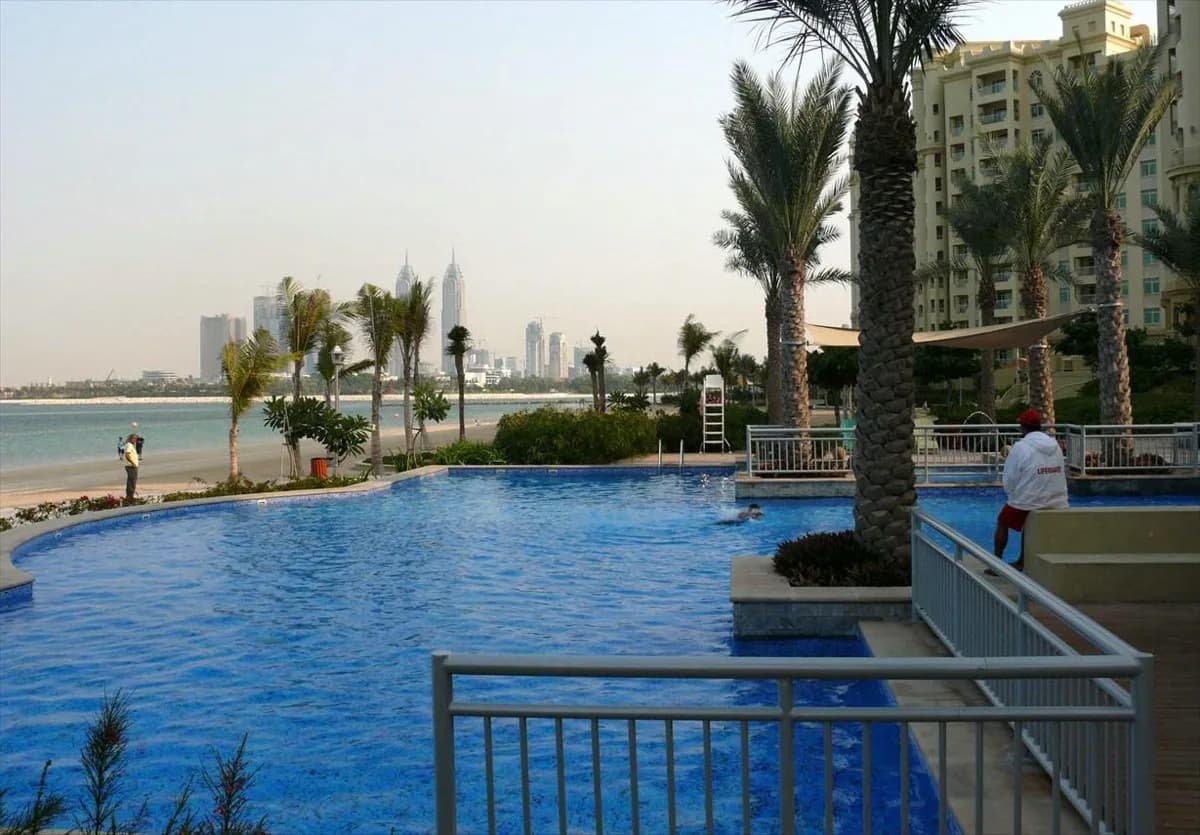 A pool and palms on Palm Jumeirah with the Dubai skyline across the water