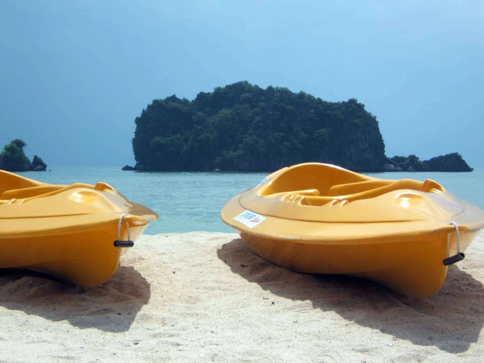 Two yellow sea canoes on the sand at Tanjung Rhu beach, with a forested islet offshore, on the north coast of Langkawi