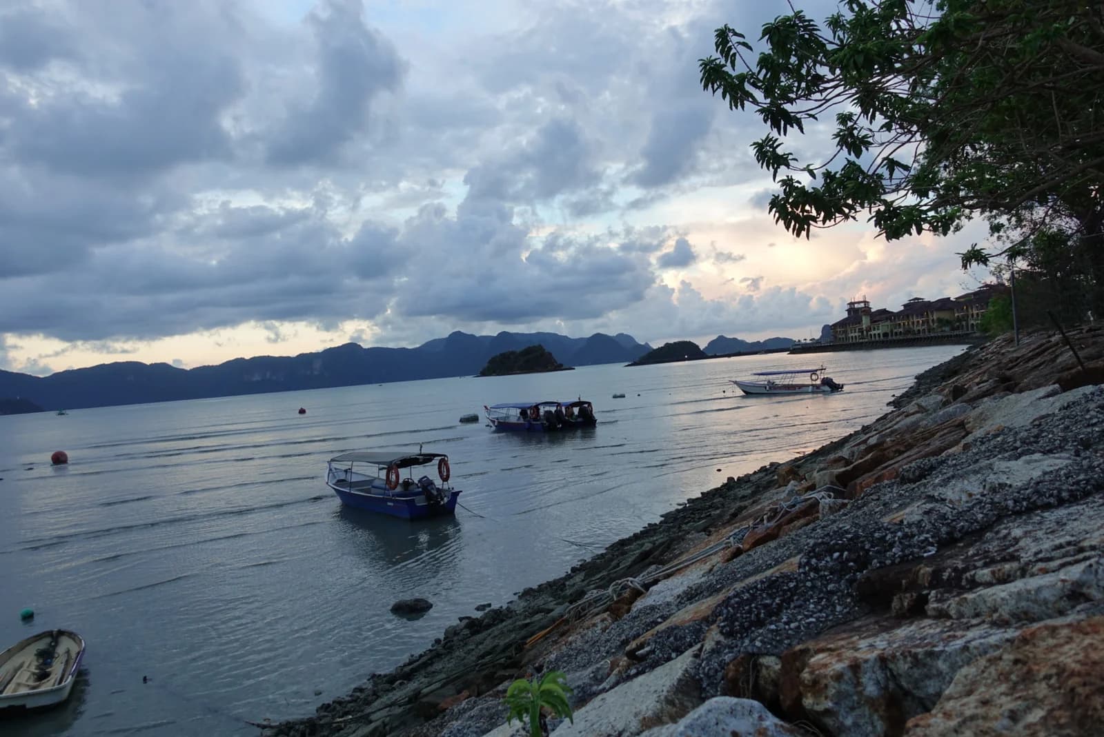 Fishing boats in the bay below the wooded rocks at Pantai Tengah, Langkawi, at dawn