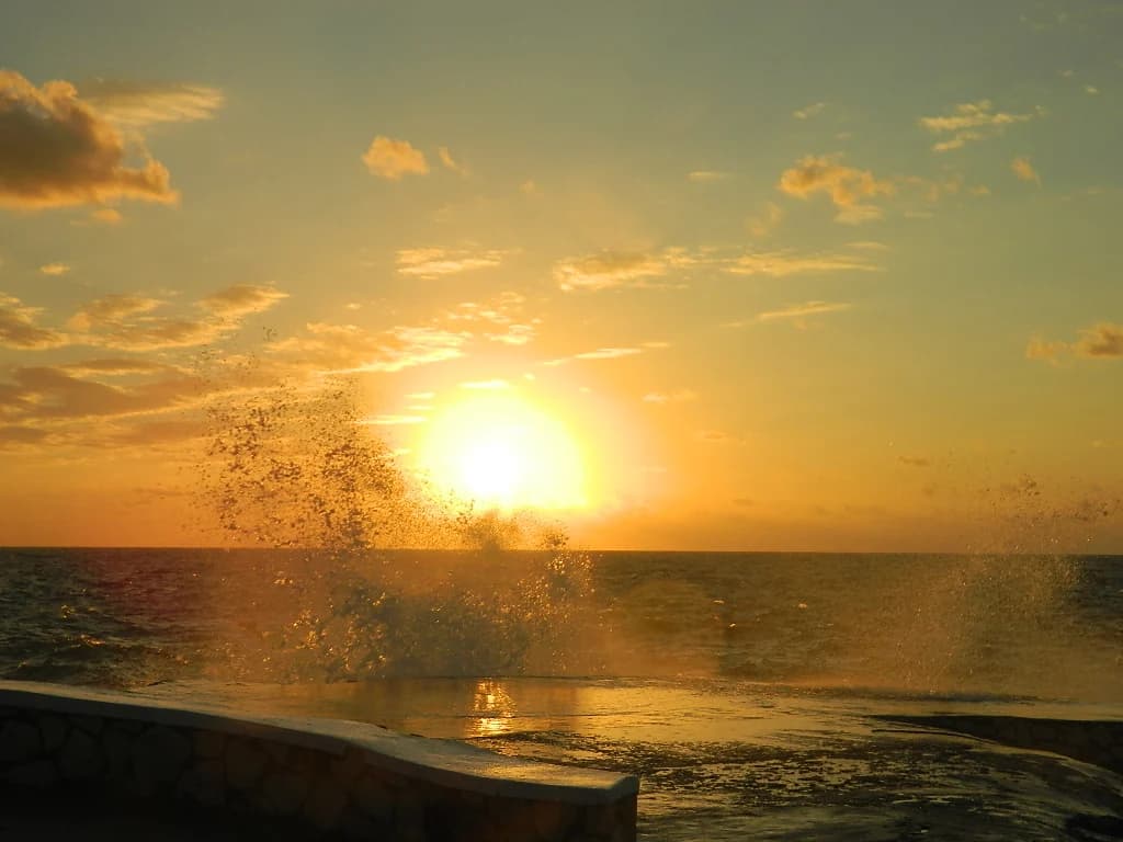 A wave breaking against the sea wall on Negril's rocky shore at sunset