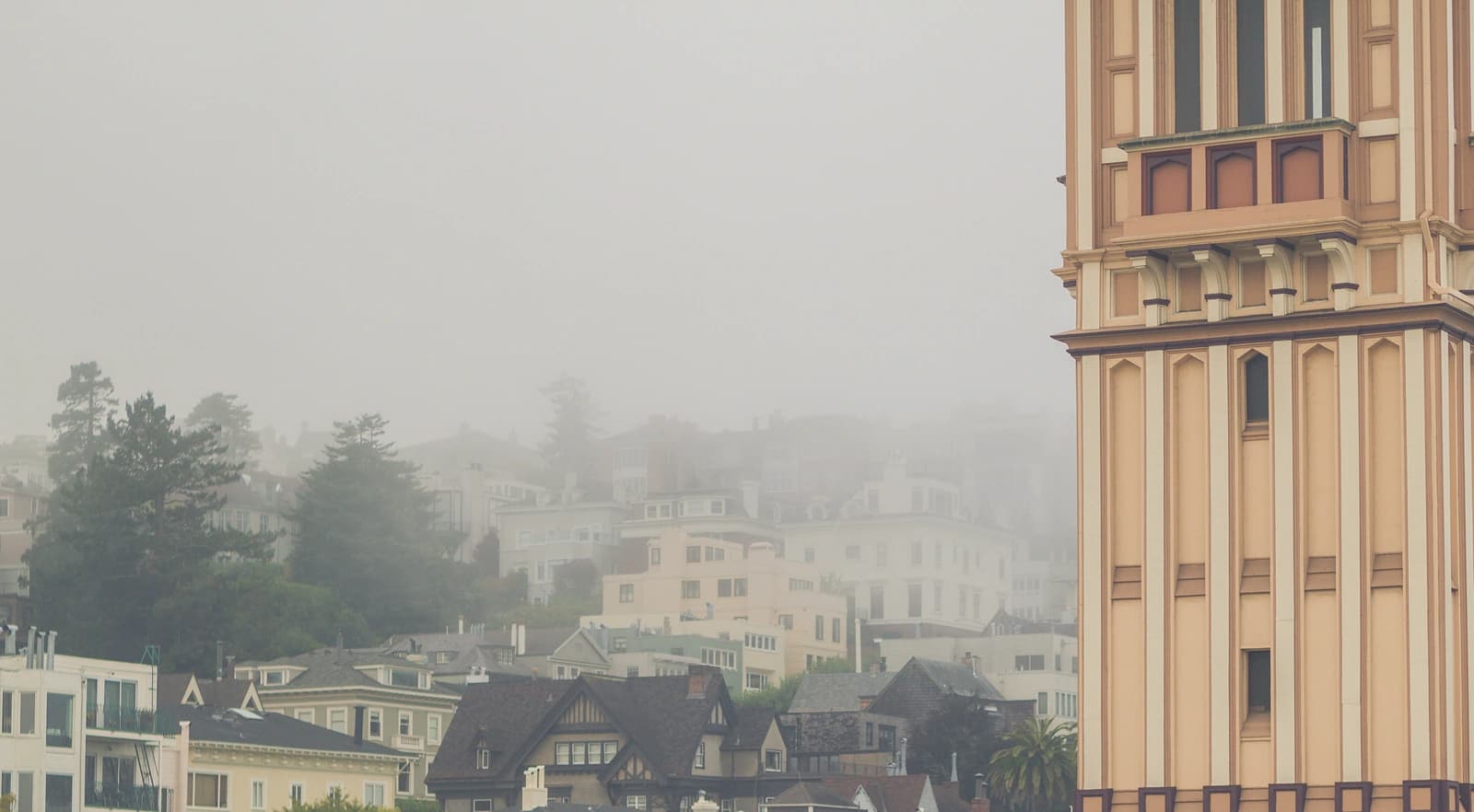 Fog drifts over Cow Hollow rooftops beside the tower of St Vincent de Paul Church