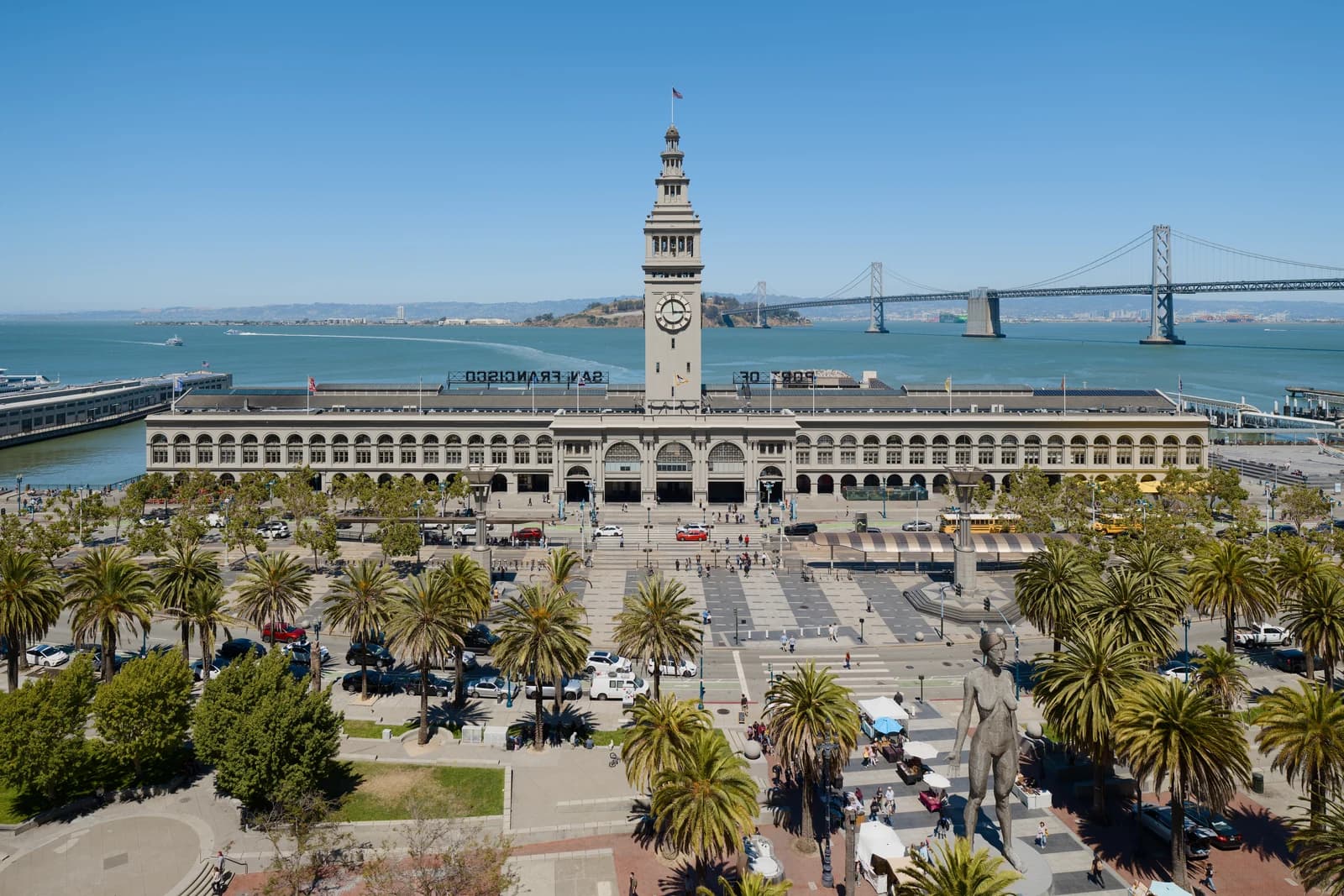 The Ferry Building clock tower and palm-lined Embarcadero plaza with the Bay Bridge behind
