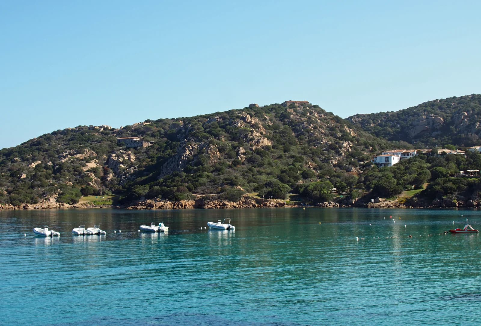 Clear water and moored boats in a bay at Baja Sardinia, below the granite hills of the Gulf of Arzachena