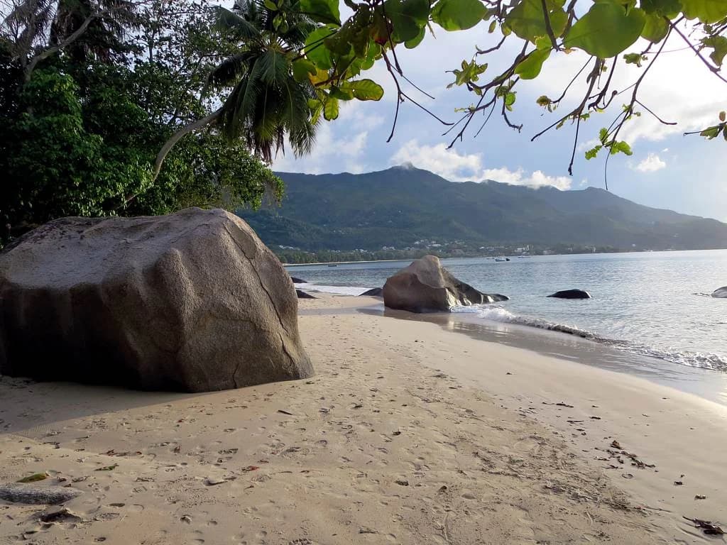 Beau Vallon bay on Mahé's north-west coast, with a granite boulder on the sand and the hills behind