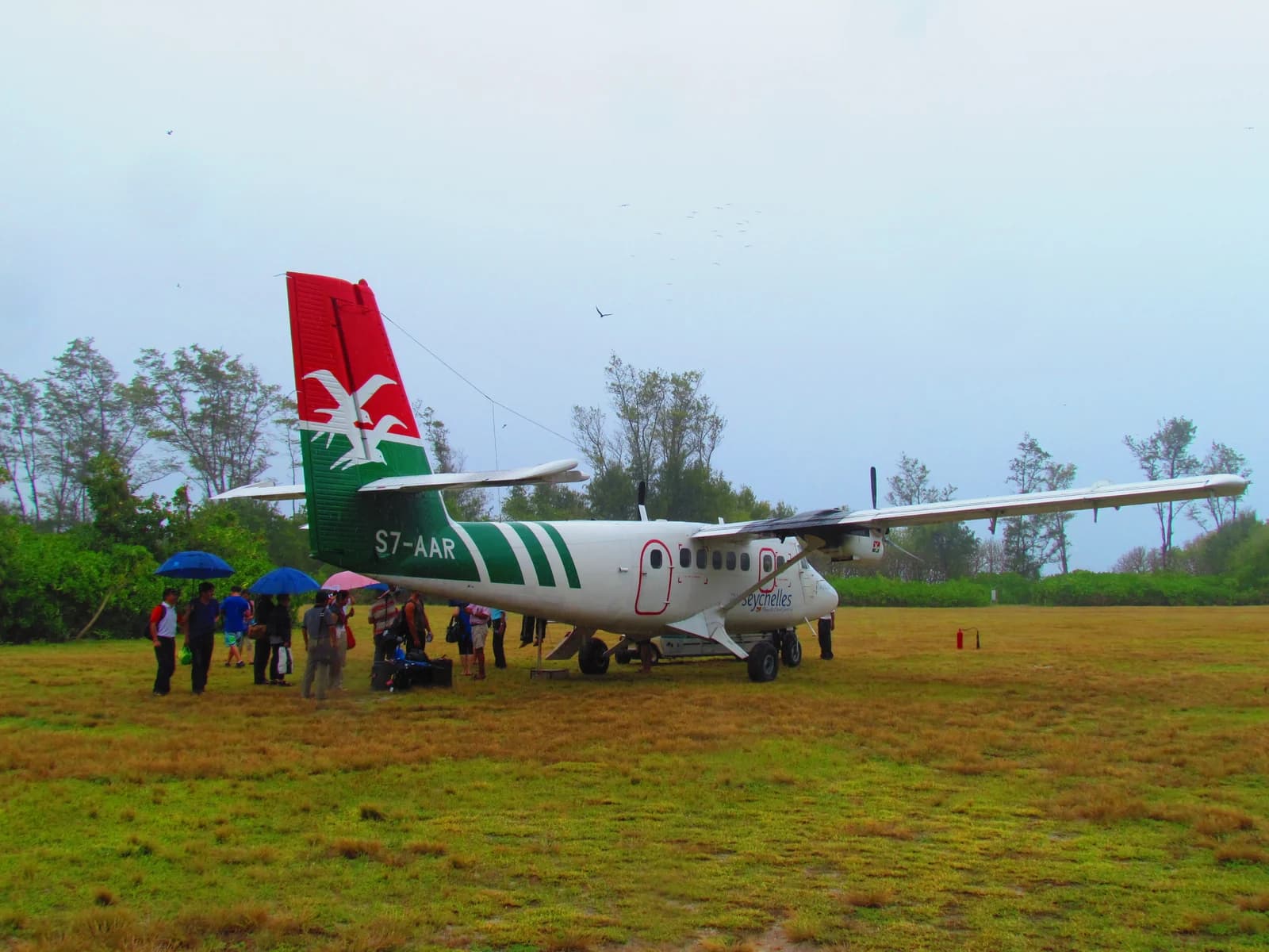 A Twin Otter on the grass airstrip at Bird Island, with arriving passengers on the field