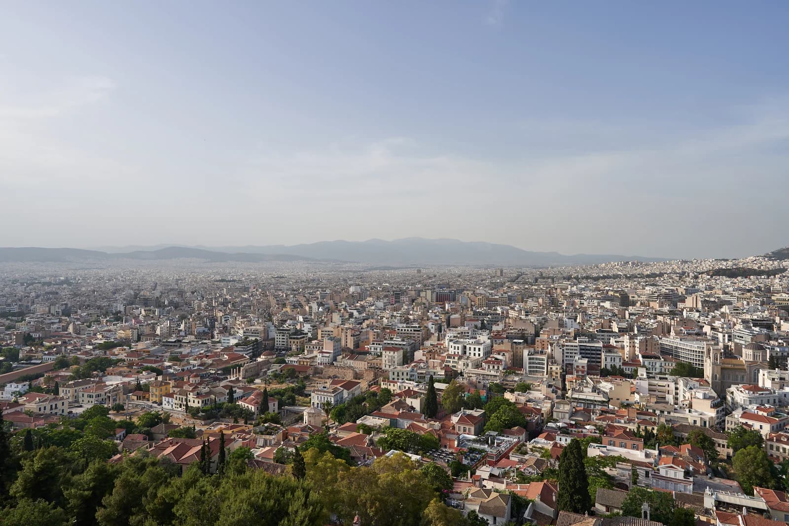 Athens seen from the Acropolis, low white buildings filling the basin below with Lycabettus hill rising behind them