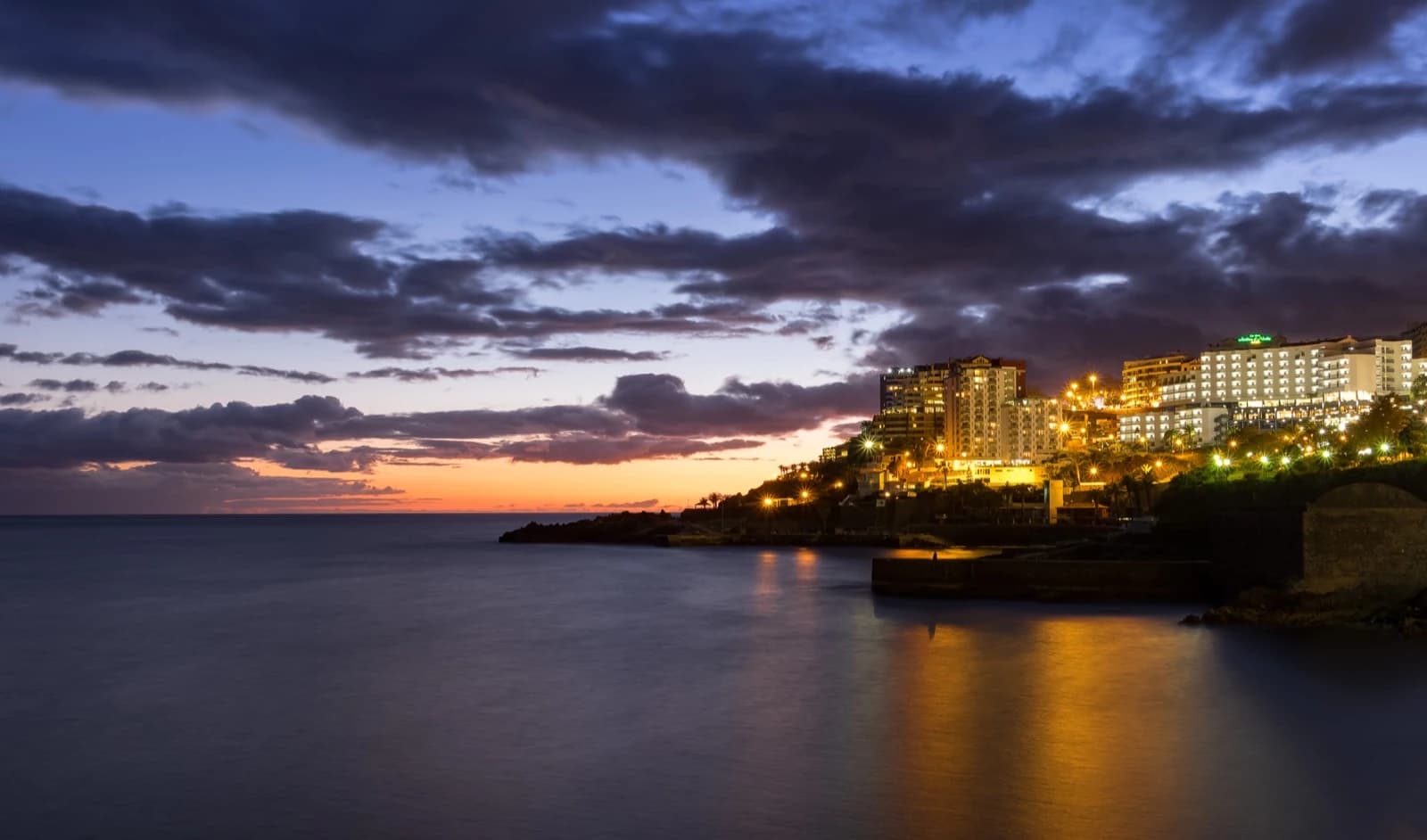 Funchal's seafront hotels lit up above the Atlantic at sunset, seen from the Lido viewpoint