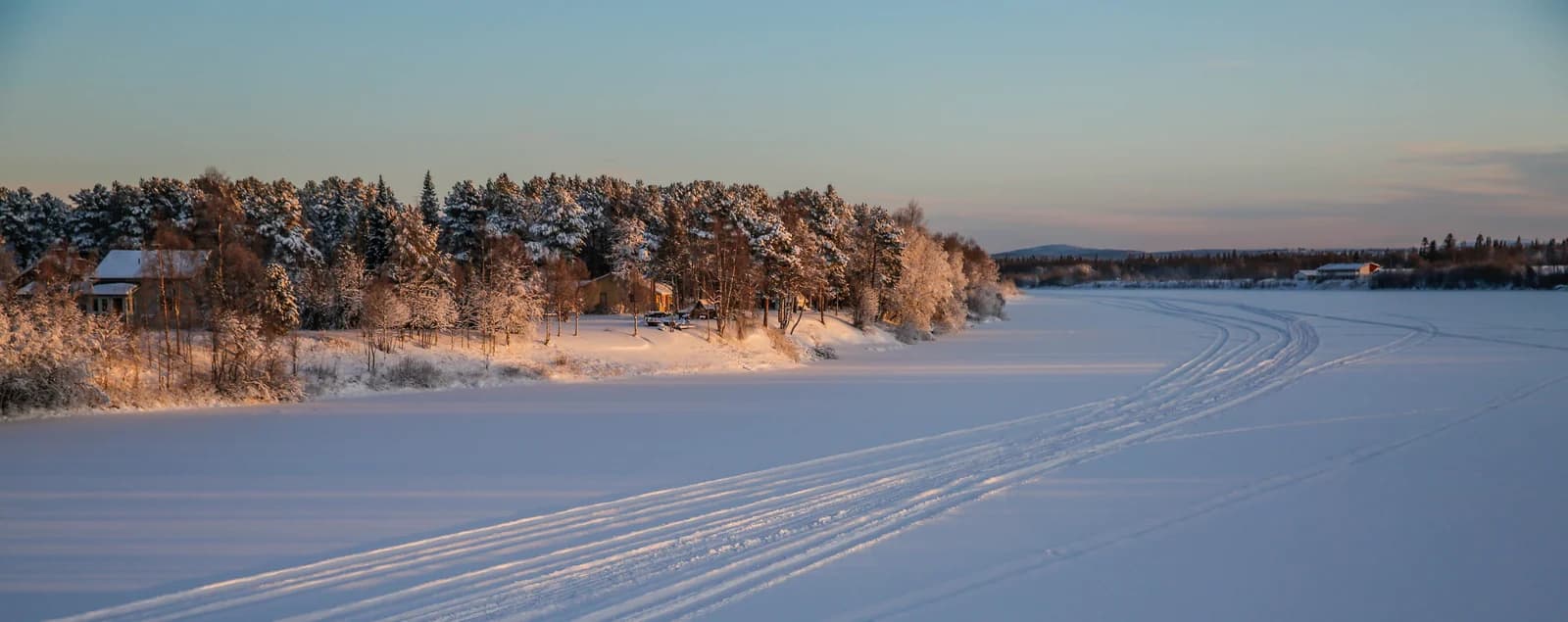 The frozen Ivalojoki river beside pine forest and wooden houses at Ivalo in low winter sun