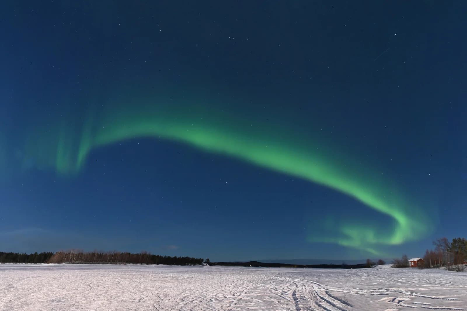 Green aurora bright enough to outshine a near full moon over the landscape at Inari in Finnish Lapland