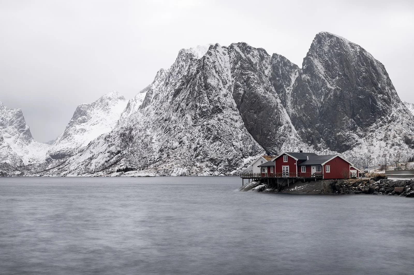 A red-painted wooden cabin at the water edge below steep rock at Hamnoy in Lofoten
