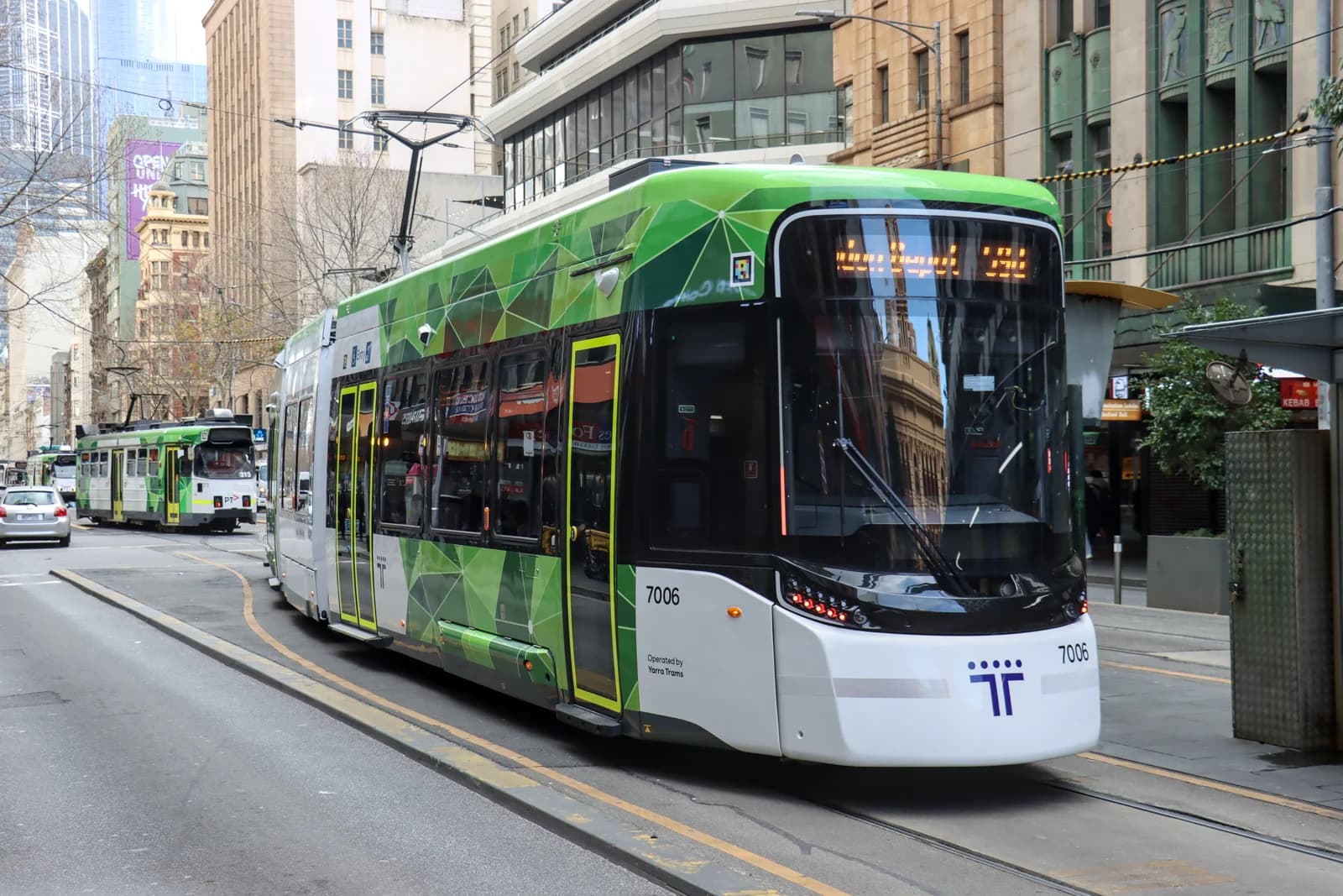 A Melbourne tram in Public Transport Victoria livery running along a city street between office blocks