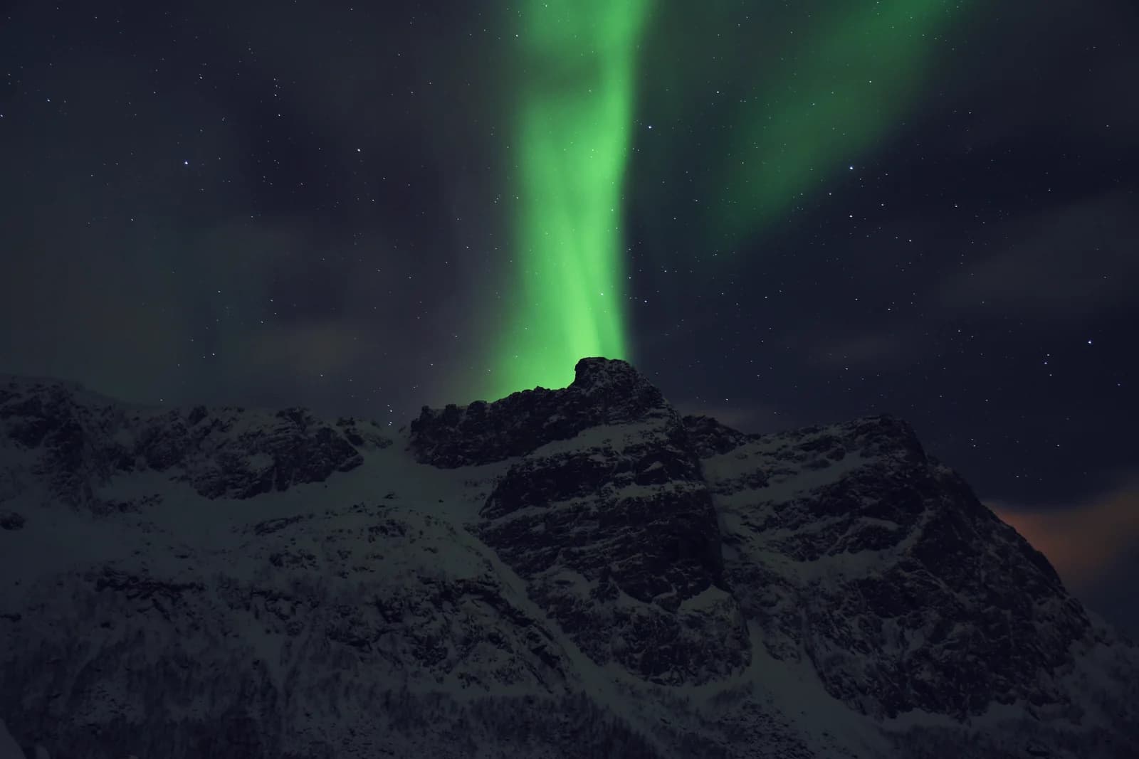 A green aurora arc over a snow covered mountain outside Tromso on a clear winter night