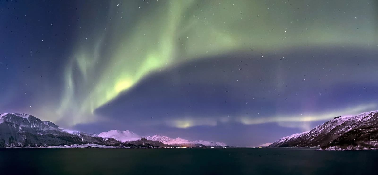 Green aurora over Lyngenfjorden in northern Norway, the fjord water still below snow covered peaks