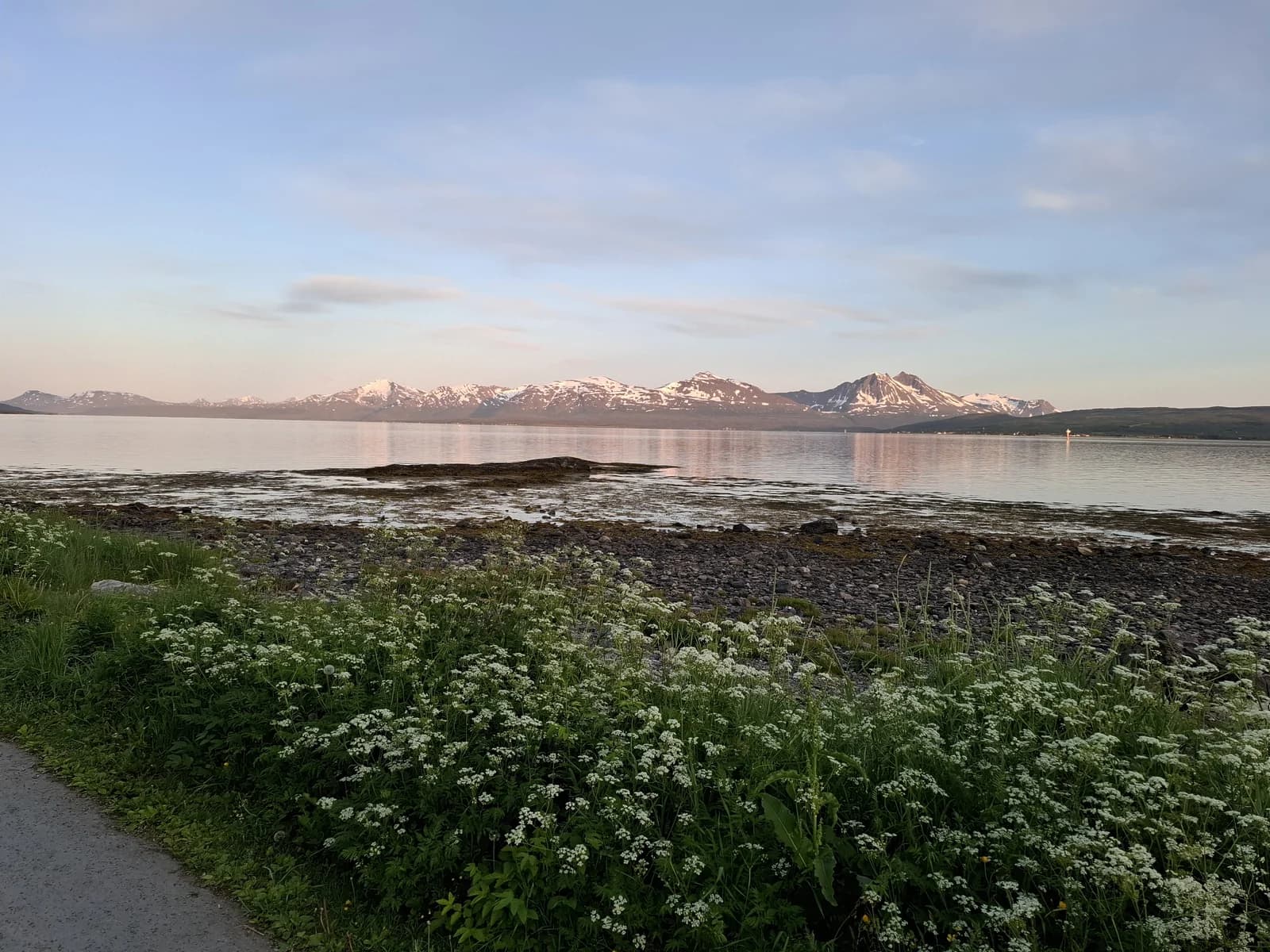Calm water and snow capped peaks in the fjord country outside Tromso under a soft evening sky
