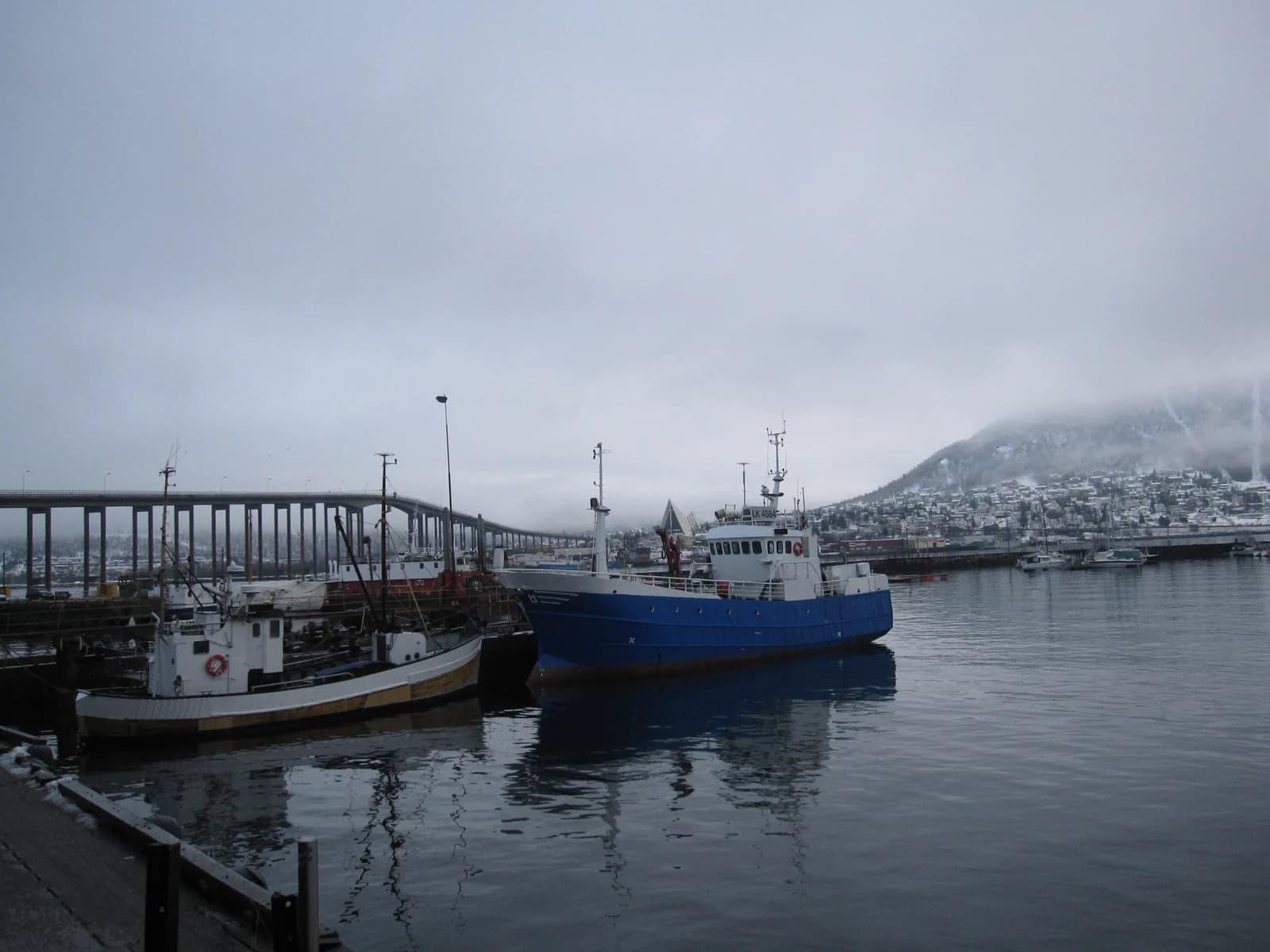 Fishing boats moored on the Tromso harbour front with the Tromso bridge and the mainland behind