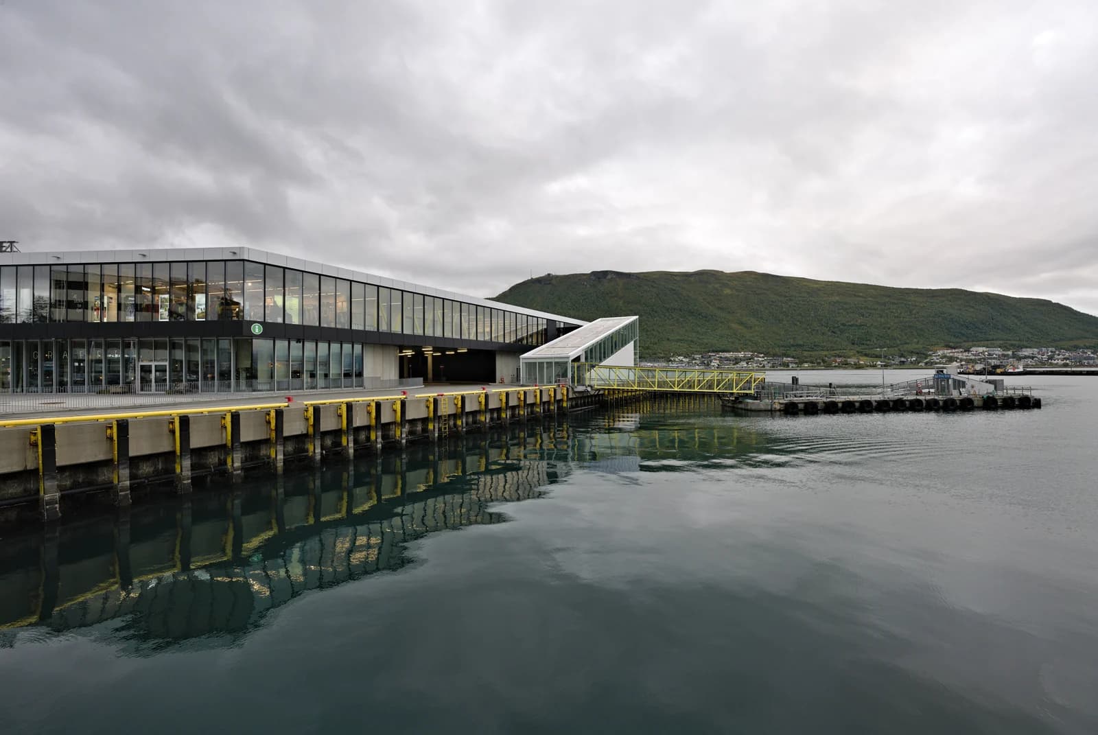The glass terminal building on the Tromso quayside, the water and the mainland hills behind it
