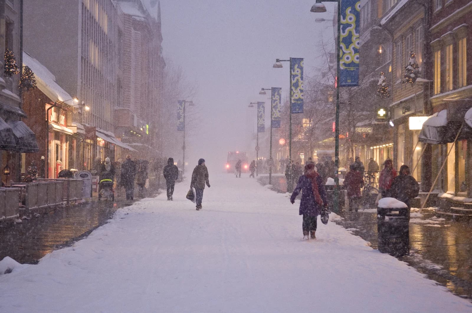 Heavy snow falling on Storgata in Tromso, shoppers walking past lit windows on the pedestrian street