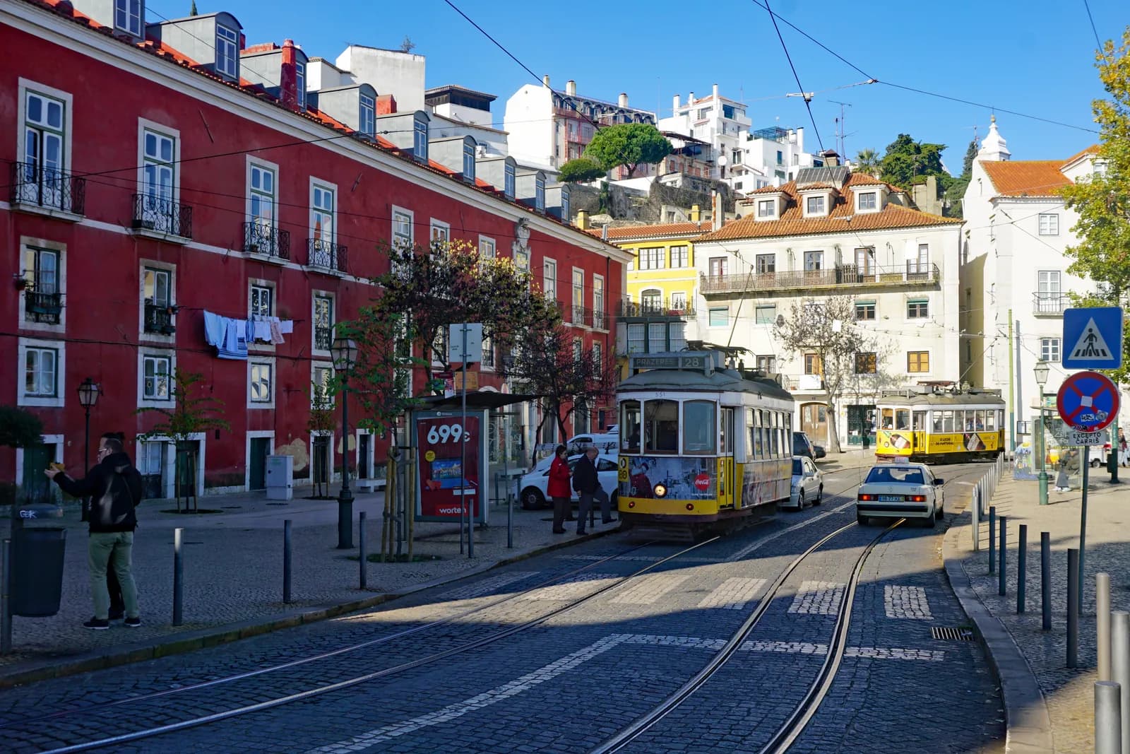 Historic yellow Tram 28 climbing a cobbled street in Lisbon's Alfama district, terracotta rooftops behind