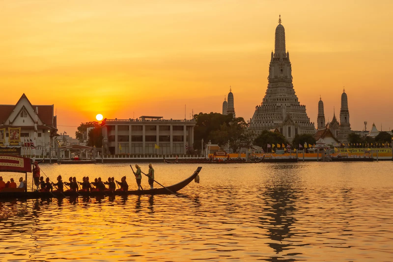 Wat Arun temple silhouetted against a golden sunset over the Chao Phraya River in Bangkok, Thailand