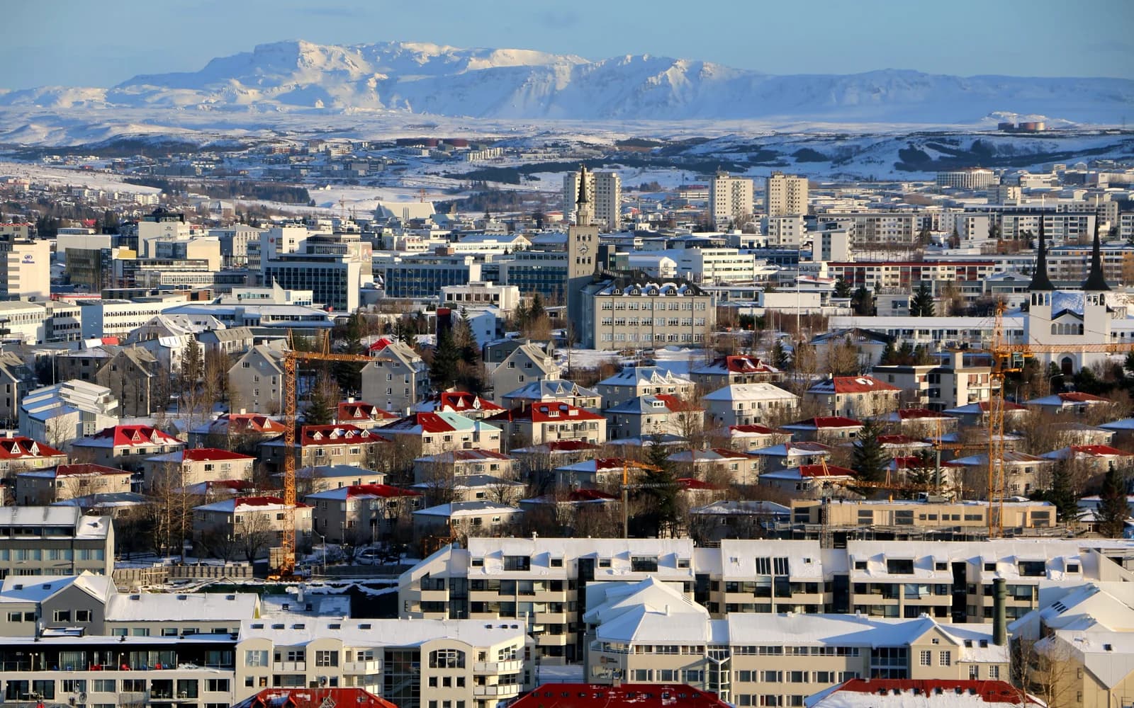 Snow on the coloured rooftops of Reykjavik with the mountains across the bay behind
