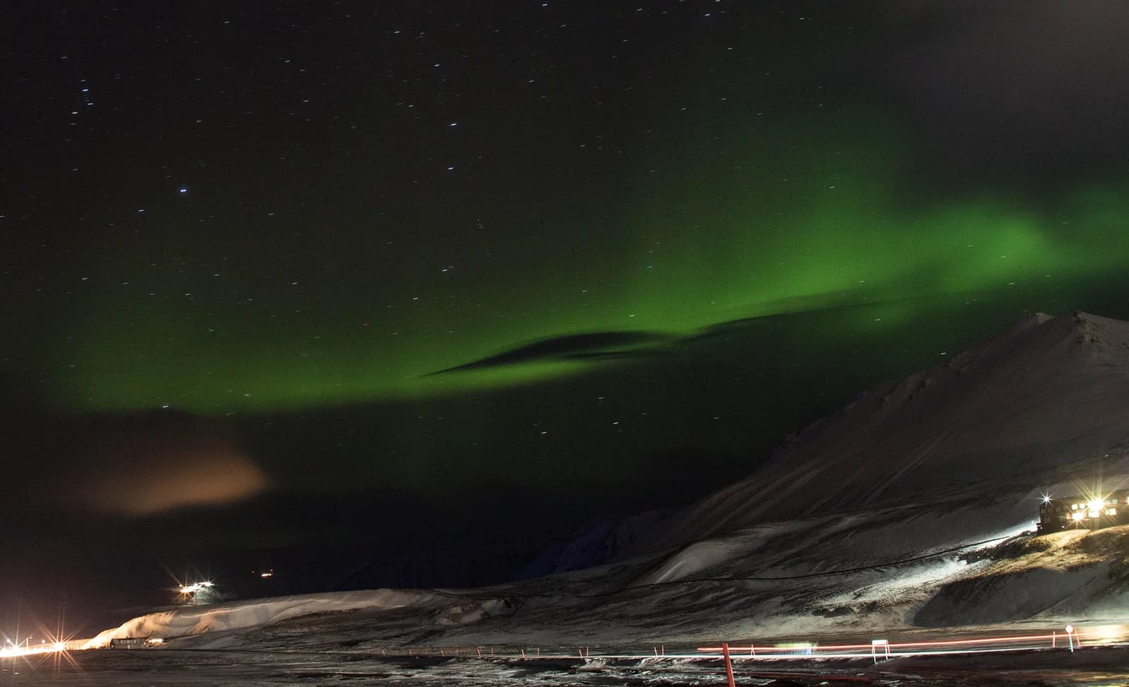 Green northern lights over the snowy mountains and settlement lights of Svalbard