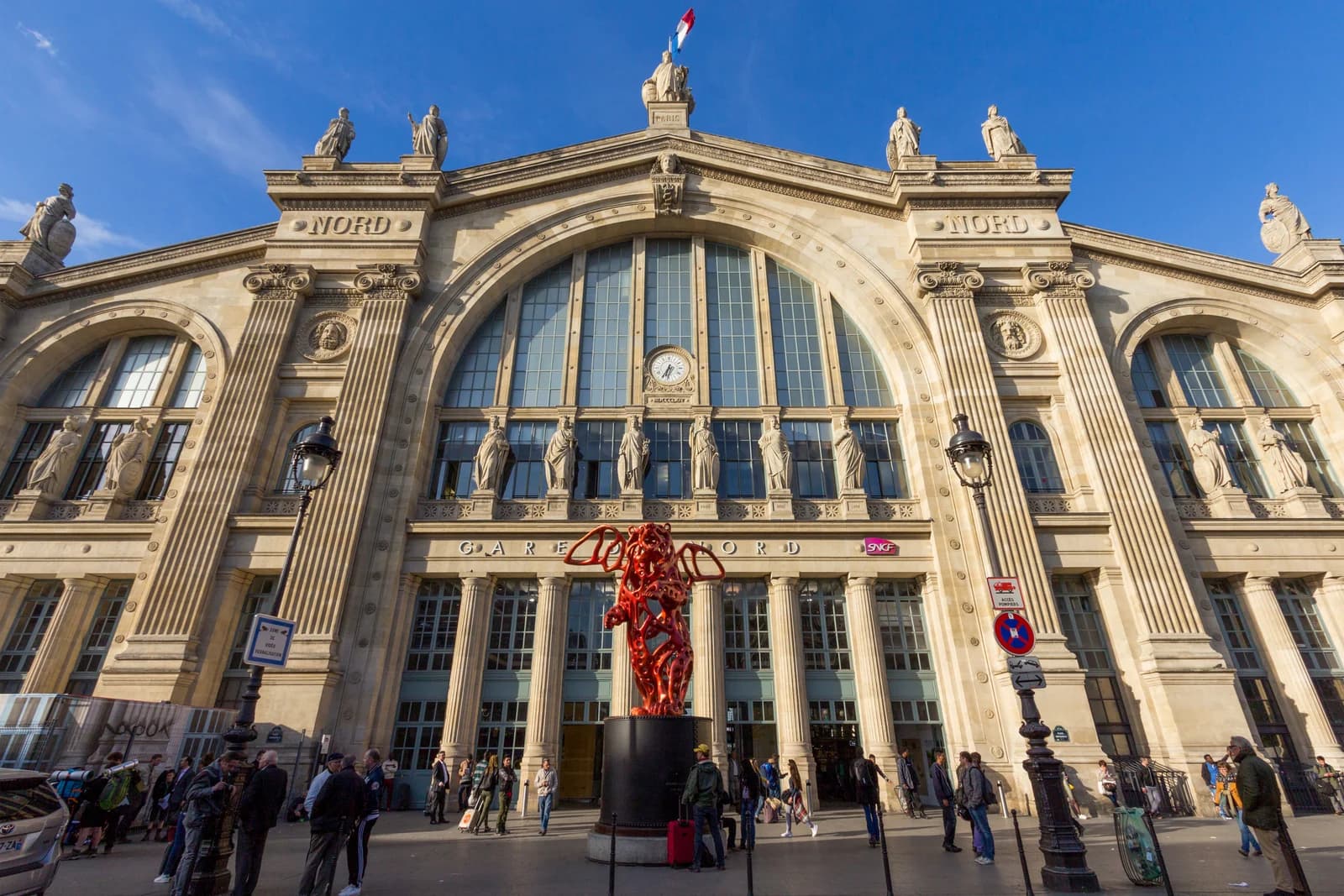 The stone facade of Gare du Nord in Paris, statues along the roofline above the arched entrances where Eurostar arrivals walk out
