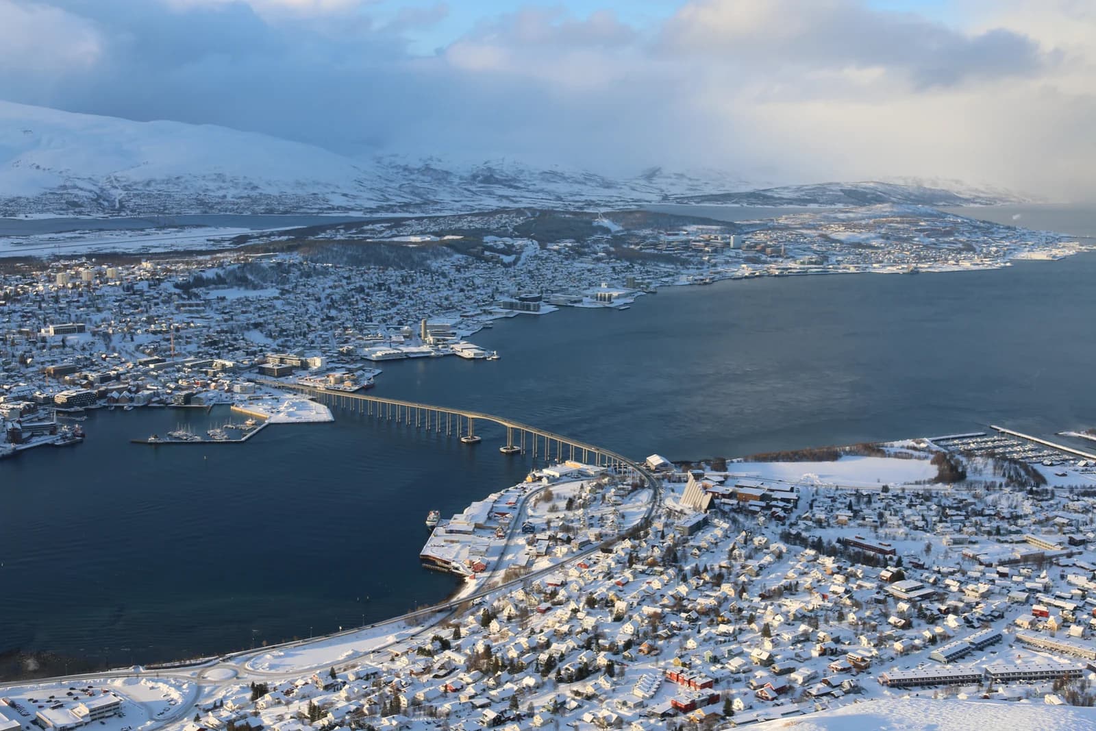 The Tromso bridge and the snow covered town seen from the mountain above it in low winter light