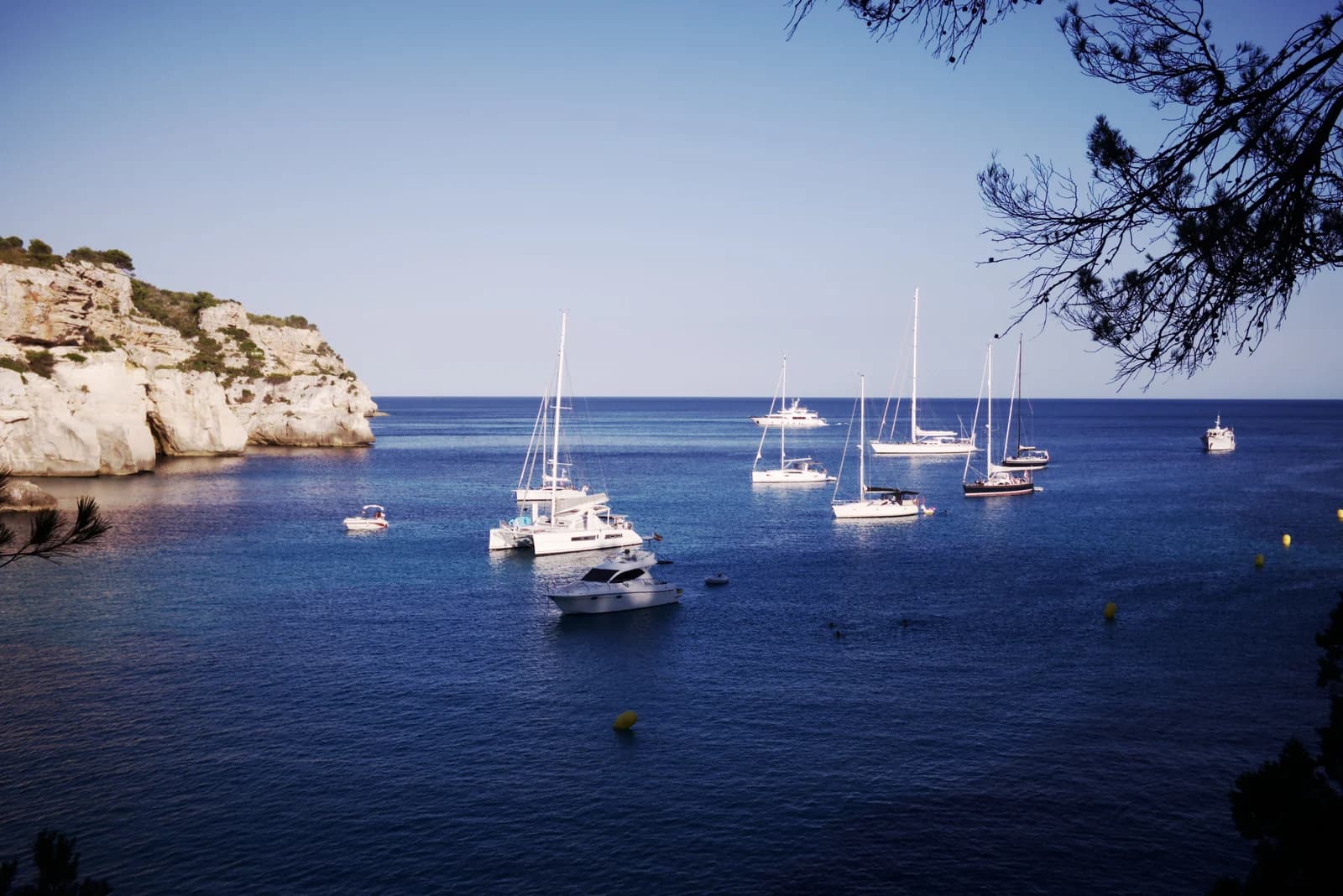 Sailboats anchored in the turquoise bay of Cala Macarella below limestone cliffs on Menorca