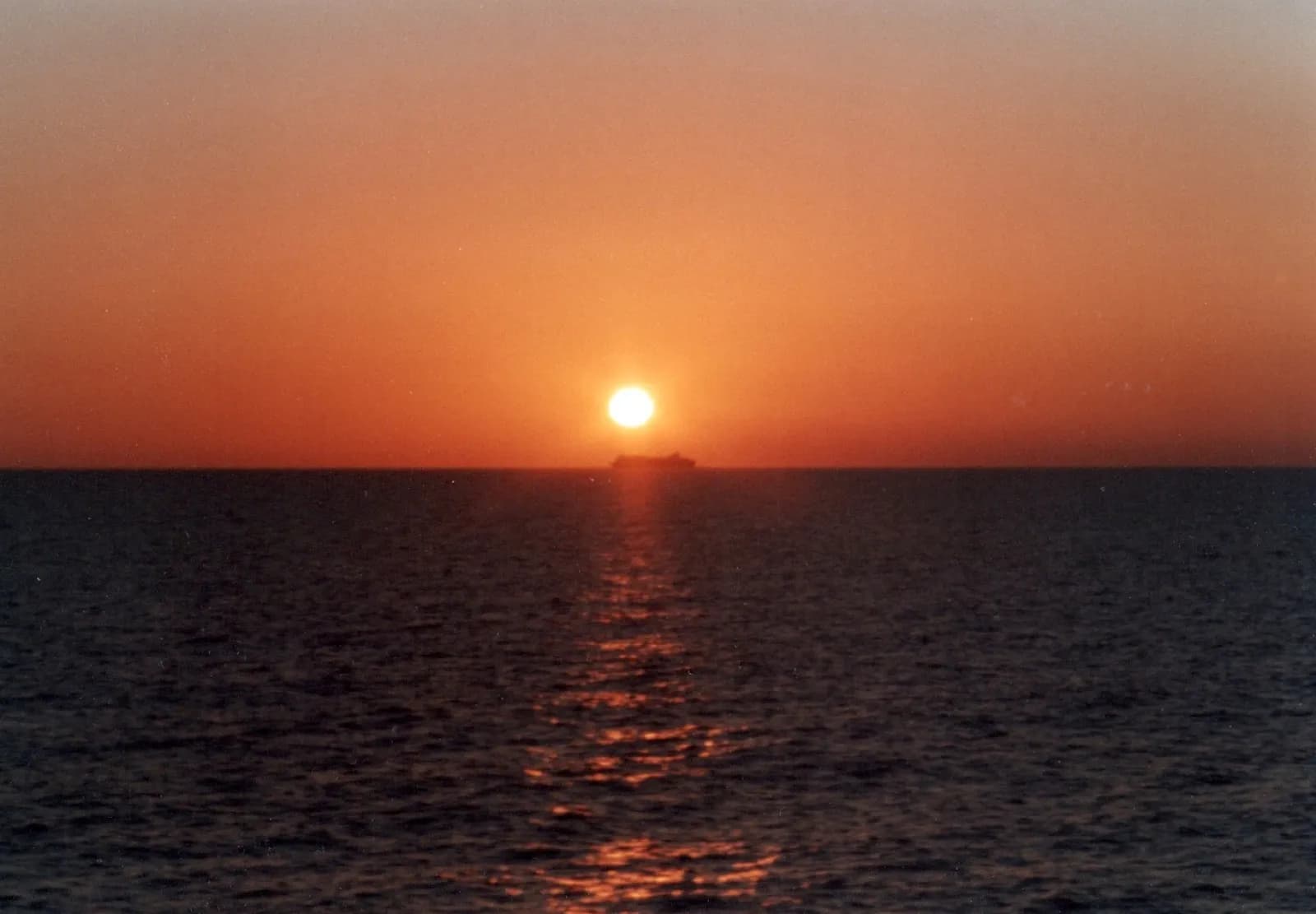 A cruise ship at sea under a burning orange sunset sky