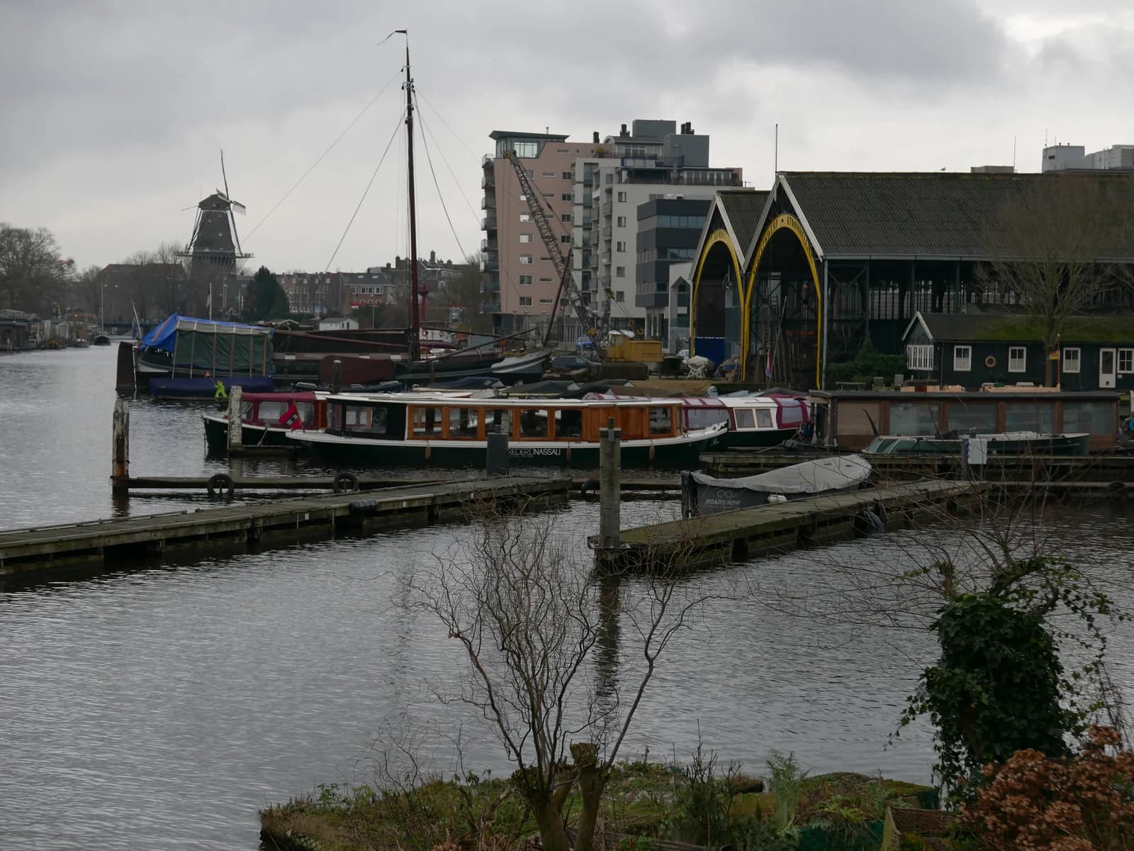 Boats moored at an old shipyard on the Nieuwe Vaart near Oostenburg, with a windmill in the distance