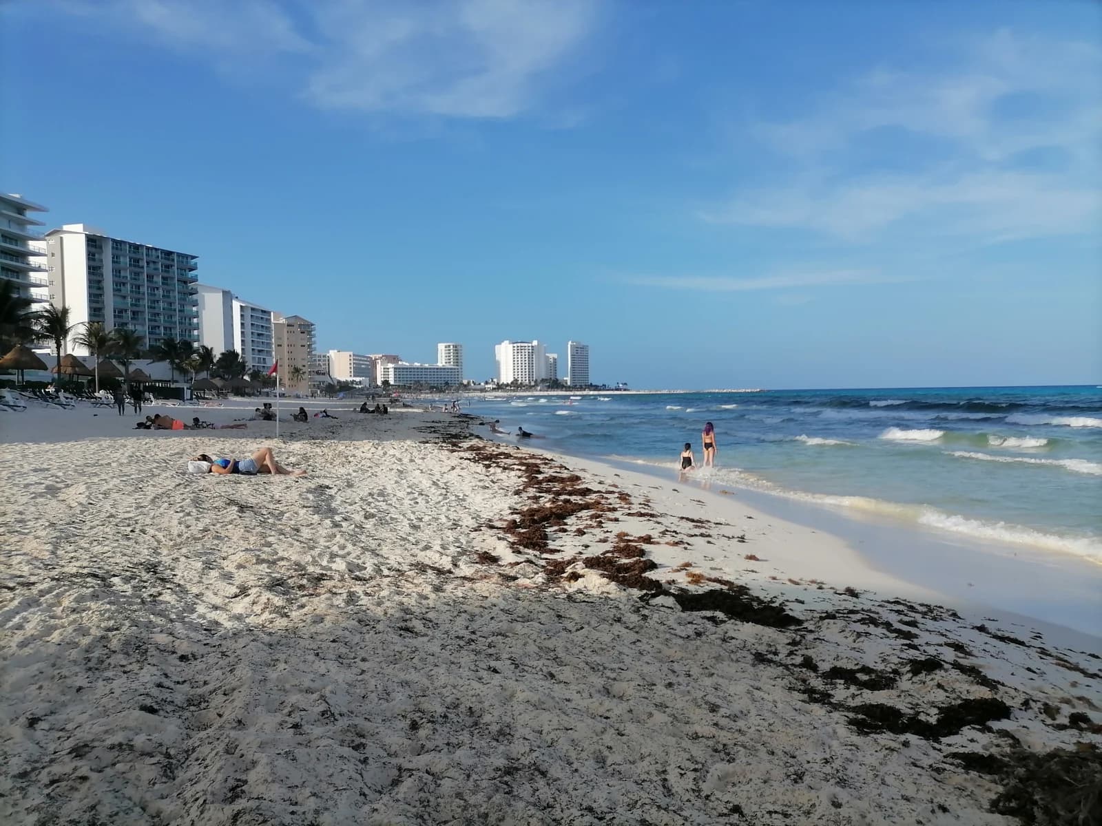 Sargassum on the sand and a red flag on the beach at Playa Delfines in Cancun