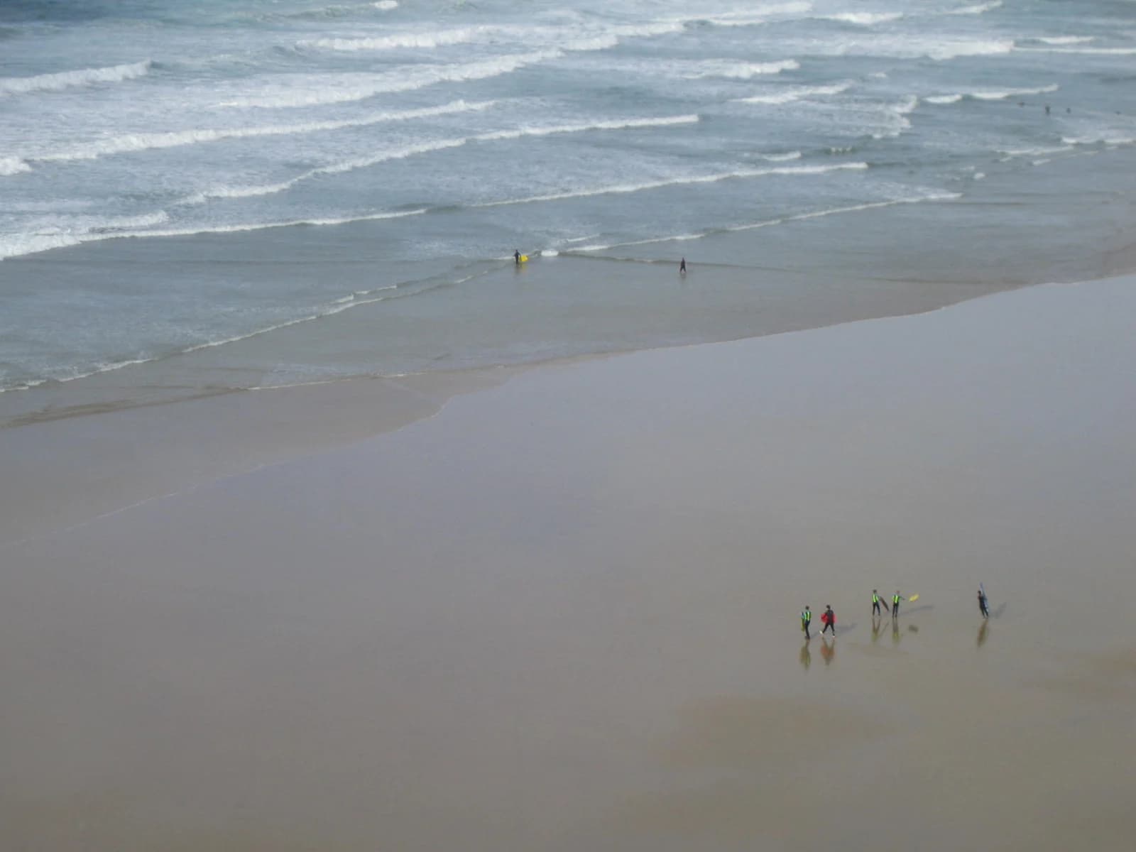 Surfers crossing the flat sand of Mawgan Porth beach in Cornwall at low tide